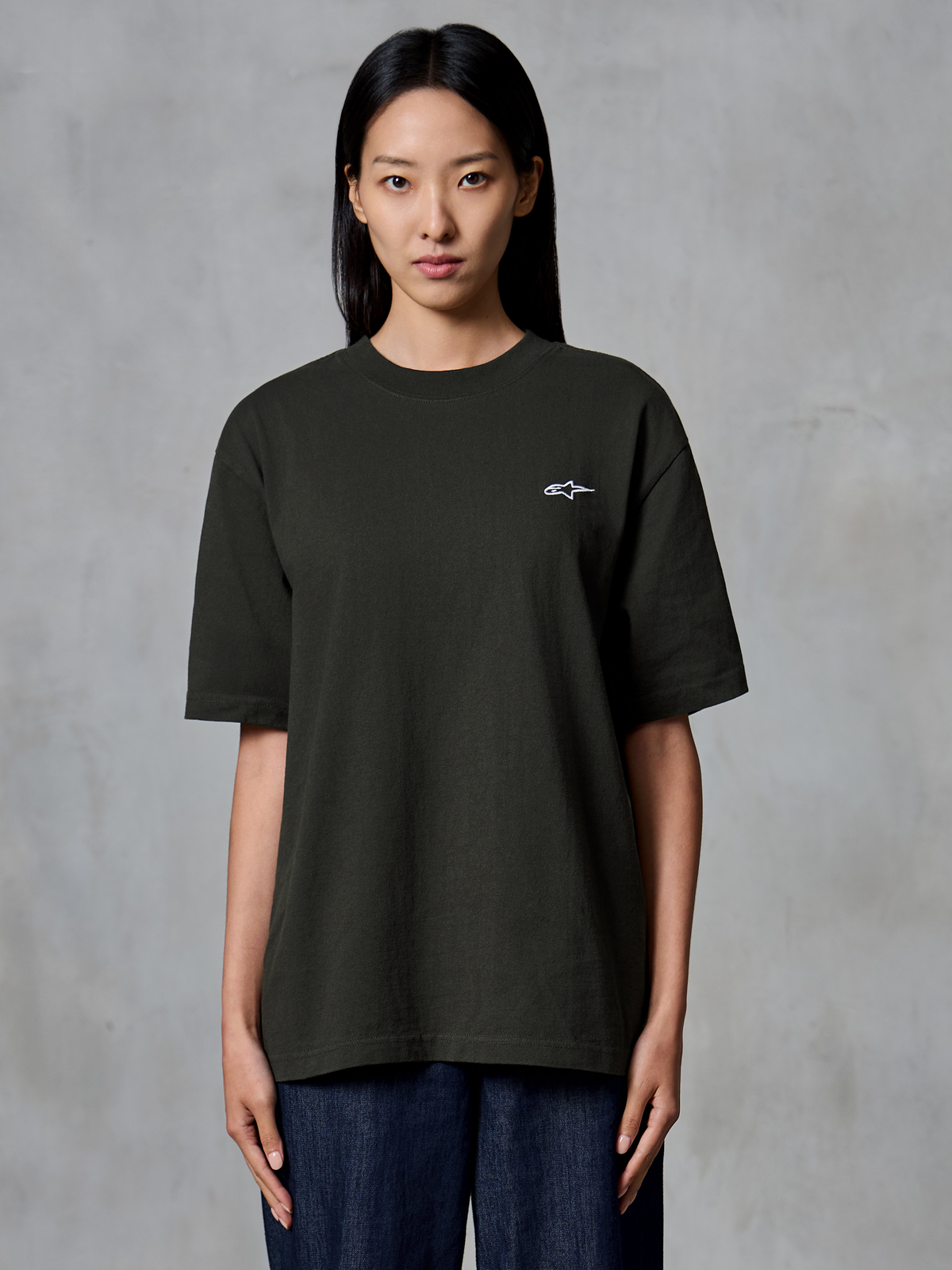 Alpinestars Essentials Ageless SS Tee, kortärmad t-shirt, Off Black, bärs av en kvinnlig modell, avslappnad passform med en liten vit Alpinestars-logotyp på vänster bröst, livsstilskläder för en avslappnad stil