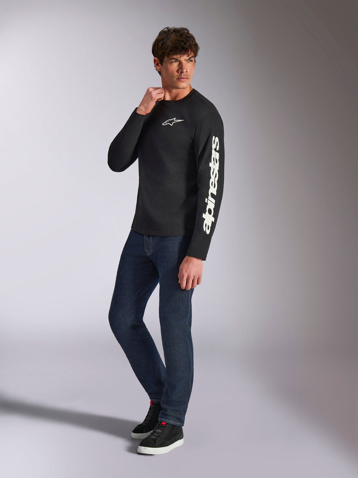 Alpinestars Trackside CSF Tee, Long Sleeve T-Shirt, Black, white vertical Alpinestars branding on sleeve and chest logo, worn by male model with dark blue jeans and sneakers, casual motorsport streetwear