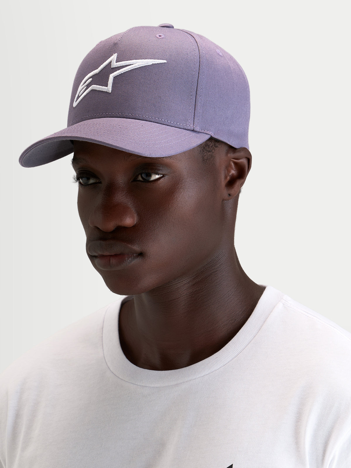 Alpinestars Ageless Snapback keps, lila keps med böjd skärm och vit broderad Astars-logotyp, bärs av modell