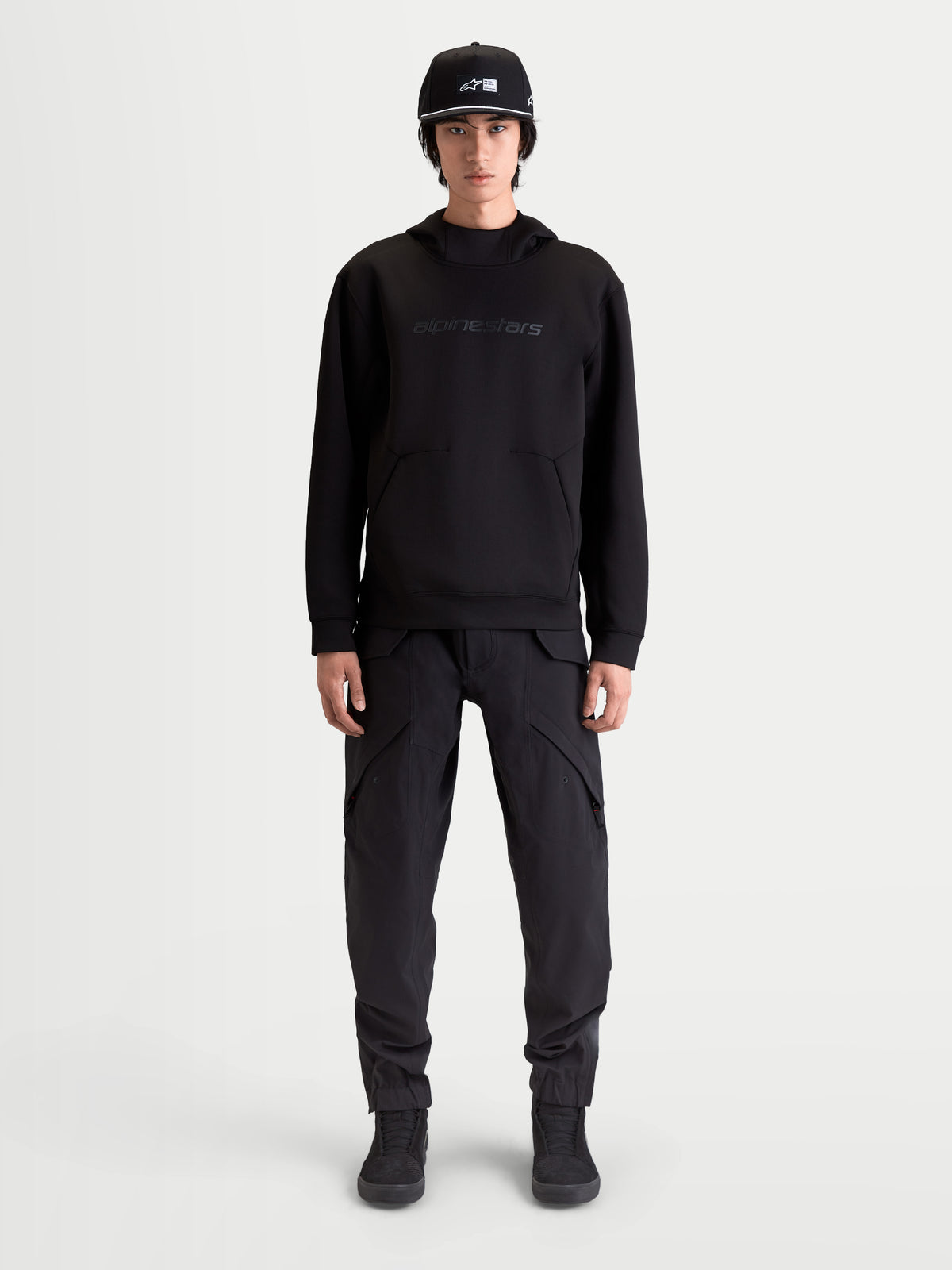Alpinestars Datrix huvtröja, premium sporttröja för herrar, svart, med tonalt Alpinestars HD-tryck, dubbelvävd tri-blend-fleece och ficka med dartdetalj, visas på modell för en motorsportinspirerad vardagsstil.