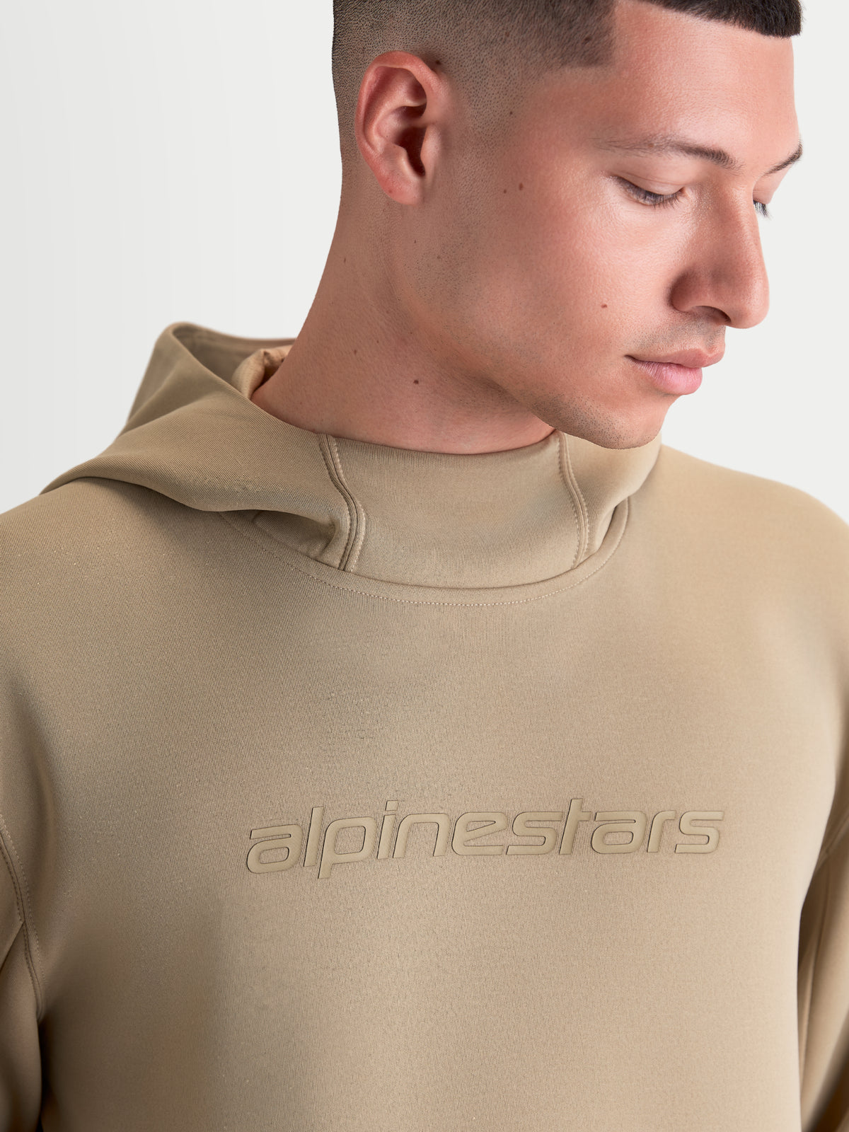 Alpinestars Datrix huvtröja, sportswear-tröja för dam och herr, brun, med tonad Alpinestars-logotyp och meshfodrad huva, närbild på modell som visar tröjans premium fleecekonstruktion