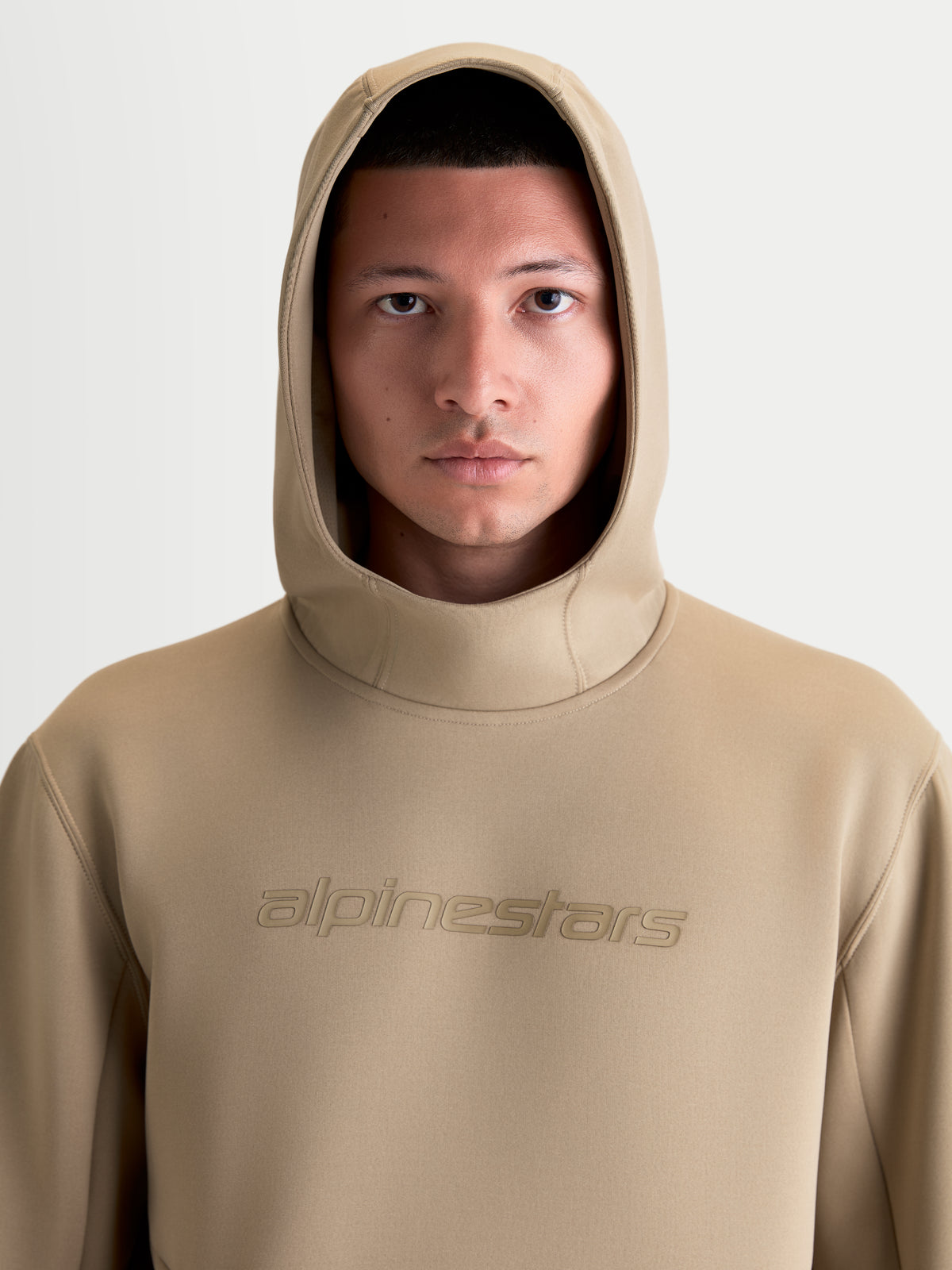 Alpinestars Datrix huvtröja, sportswear-huvtröja för herr och dam, brun, närbild på modell med huvan uppe, tonal Alpinestars-logotyp och premium tri-blend-fleece