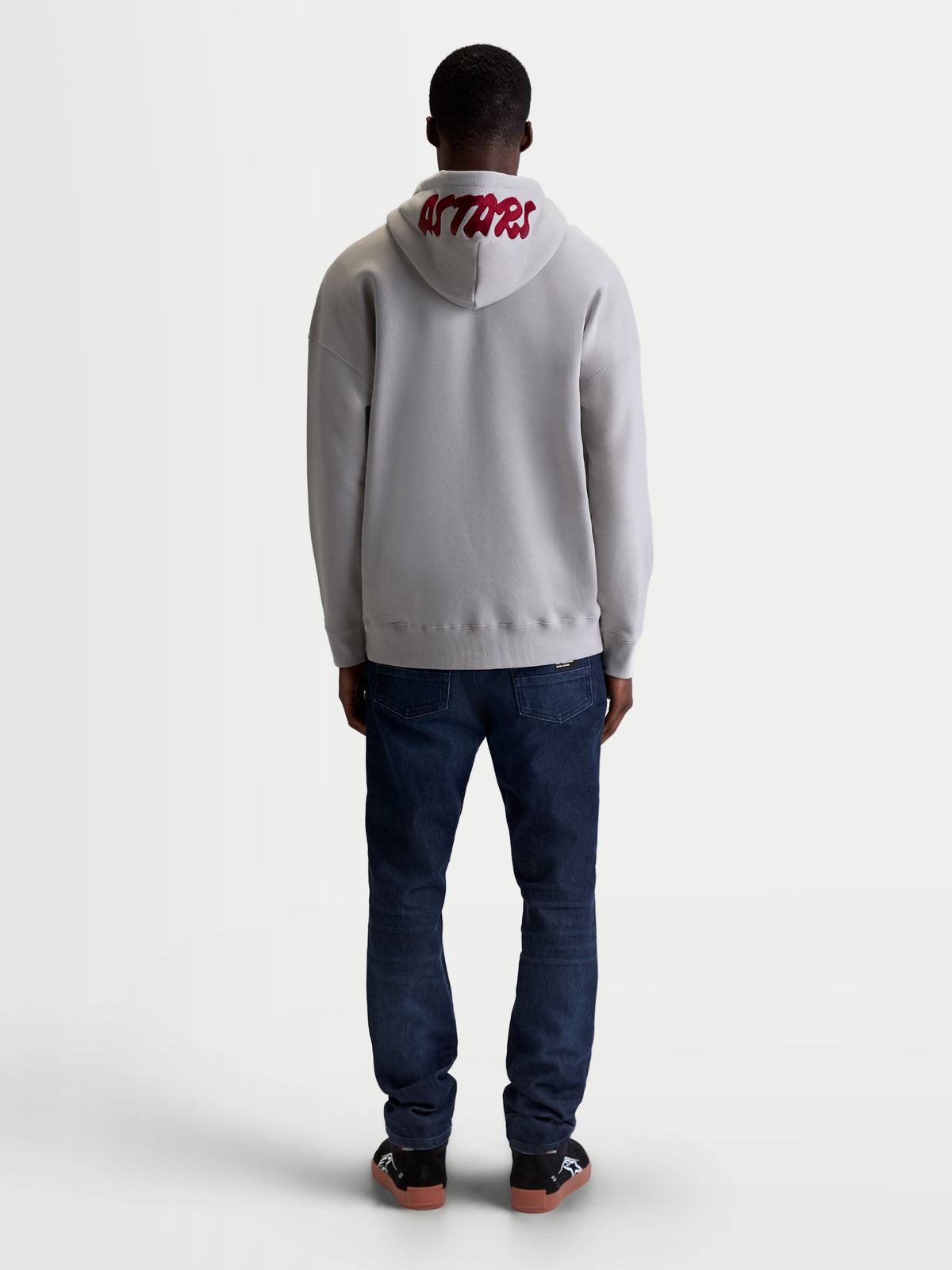 Alpinestars Pioneer Oversized Hoodie, Casual Sportswear Zip Fleece for Men and Women, Cement Gray and Red, Rear view on model highlighting red 'ASTARS' embroidered logo on the hood and relaxed oversized fit.