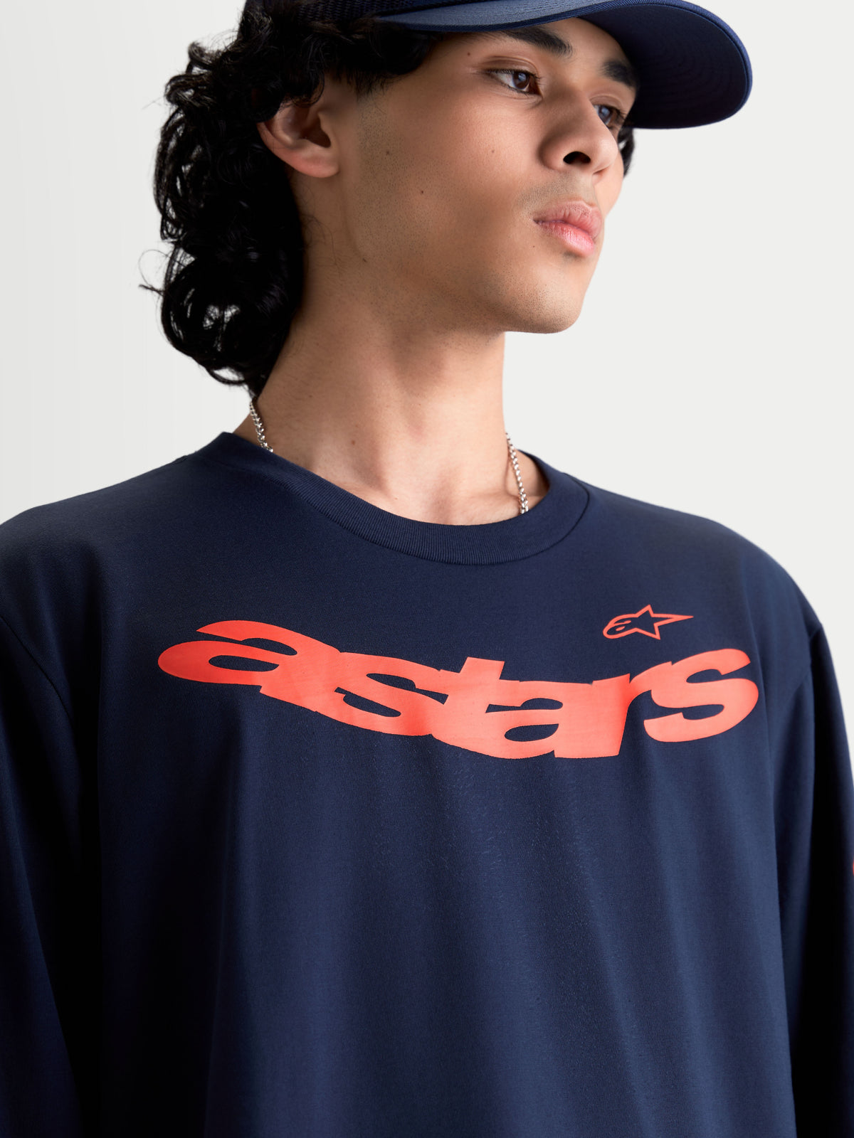 Alpinestars Velocifier CSF långärmad t-shirt, motorsportinspirerad sportswear på modell, marinblå med böjt orange Astars-tryck på bröstet, mjuk bomullsblandning.