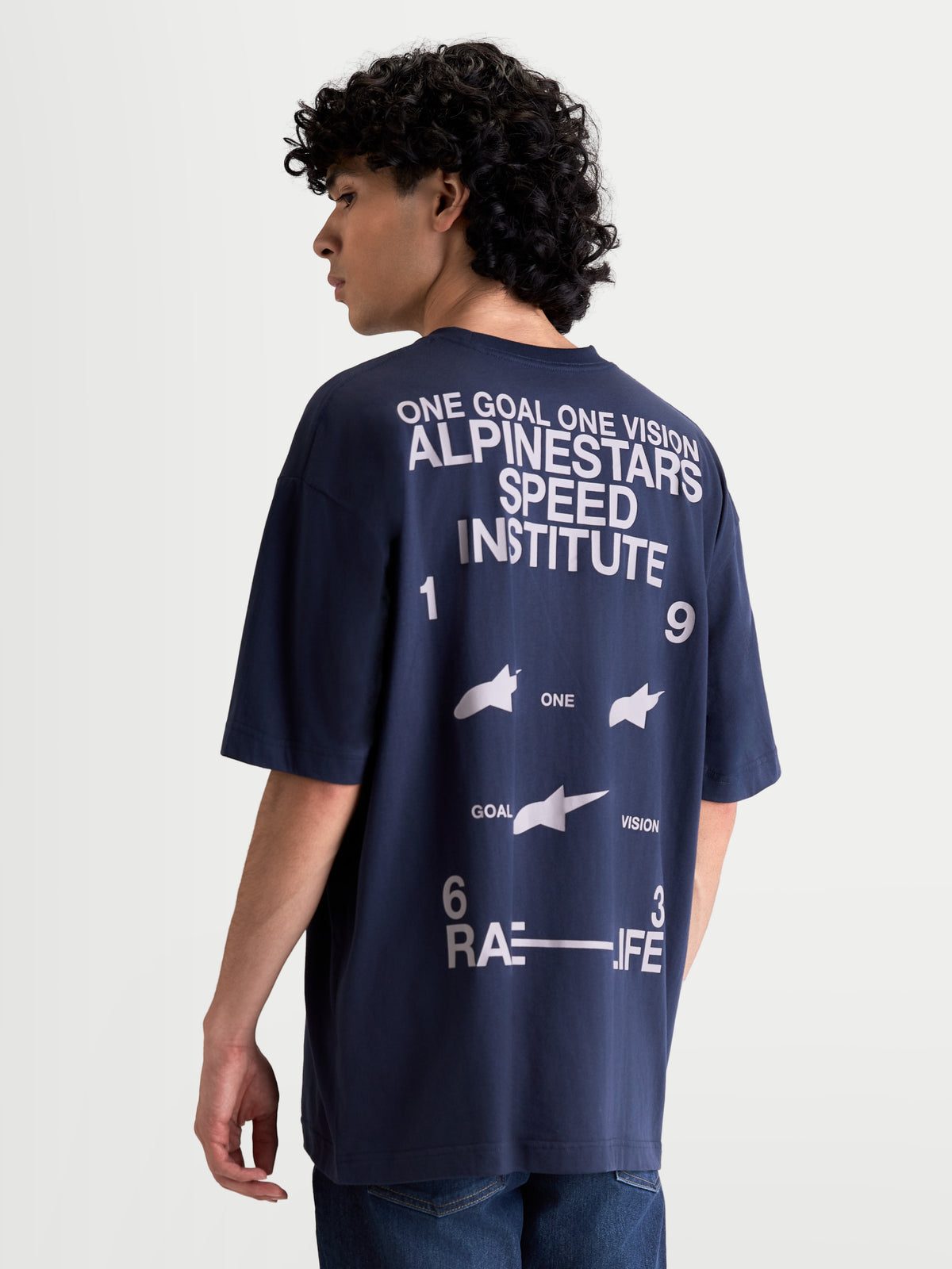 Alpinestars Institute Oversized SS CSF t-shirt, marinblå kortärmad t-shirt för herr med vitt grafiskt ryggtryck, Alpinestars Speed Institute och One Goal One Vision branding, avslappnad oversized passform, man bär tröjan sedd bakifrån.