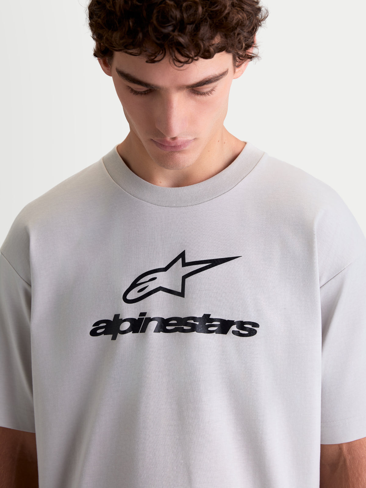 Alpinestars Prelude Oversized CSF t-shirt, kortärmad sporttröja i cementgrå med svart logotypgrafik på bröstet, oversized passform, mjuk bomull-polyesterblandning, lifestyle-topp visad på modell
