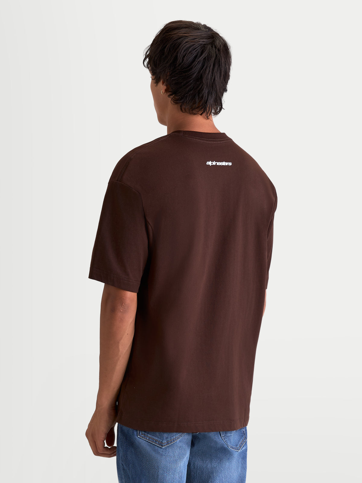 Alpinestars Prelude Oversized CSF t-shirt, brun kortärmad t-shirt i sportswear-stil, sedd bakifrån på modell med vitt Alpinestars-ordmärke på övre delen av ryggen, avslappnad oversized passform.