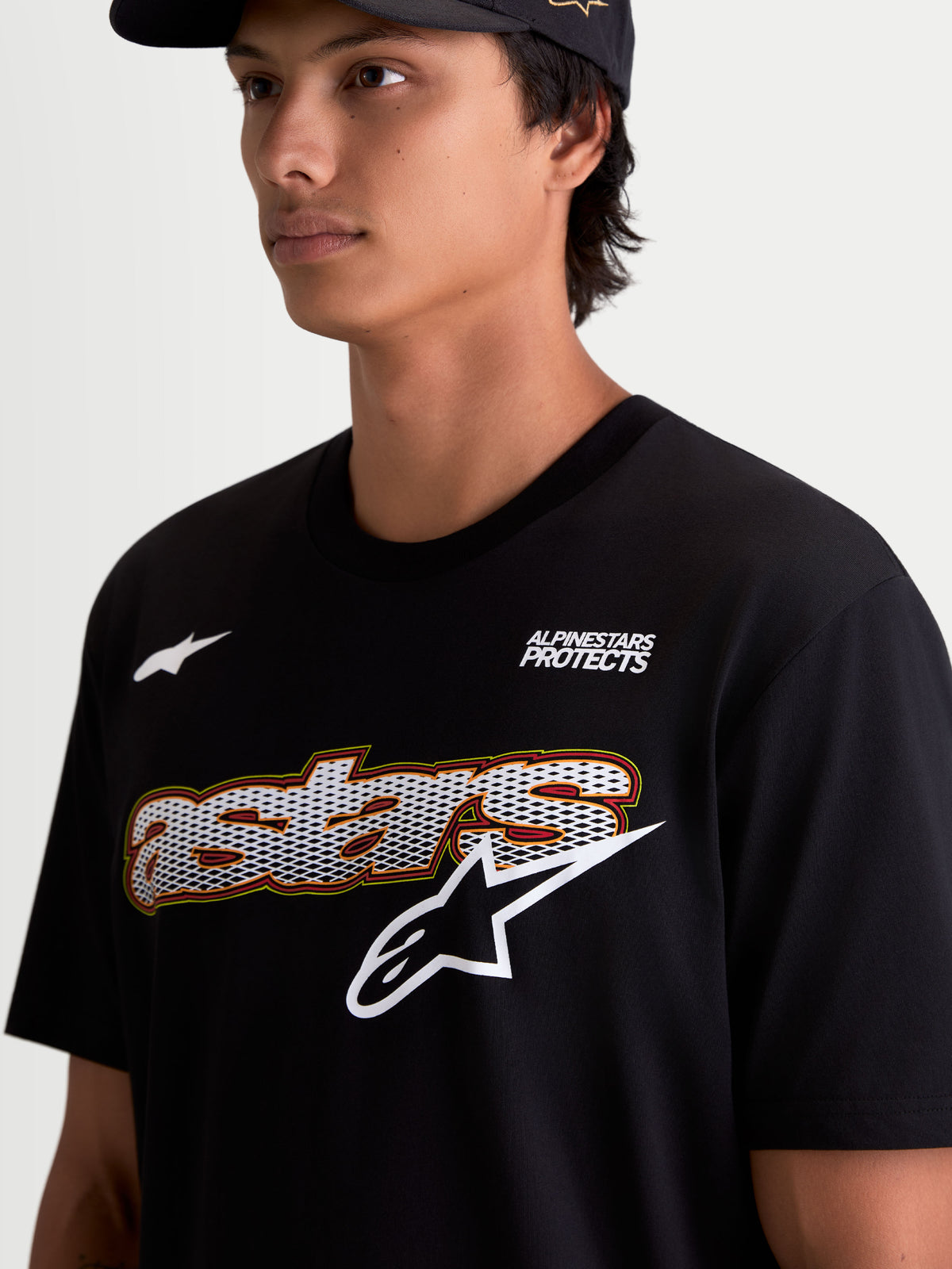 Alpinestars Cypress CSF T-shirt, kortärmad sportswear-t-shirt för herr, svart, närbild på modell som visar bröstgrafiken med meshfylld text, ”Alpinestars Protects”-branding och vit logotyp, premium bomull-polyesterblandning.
