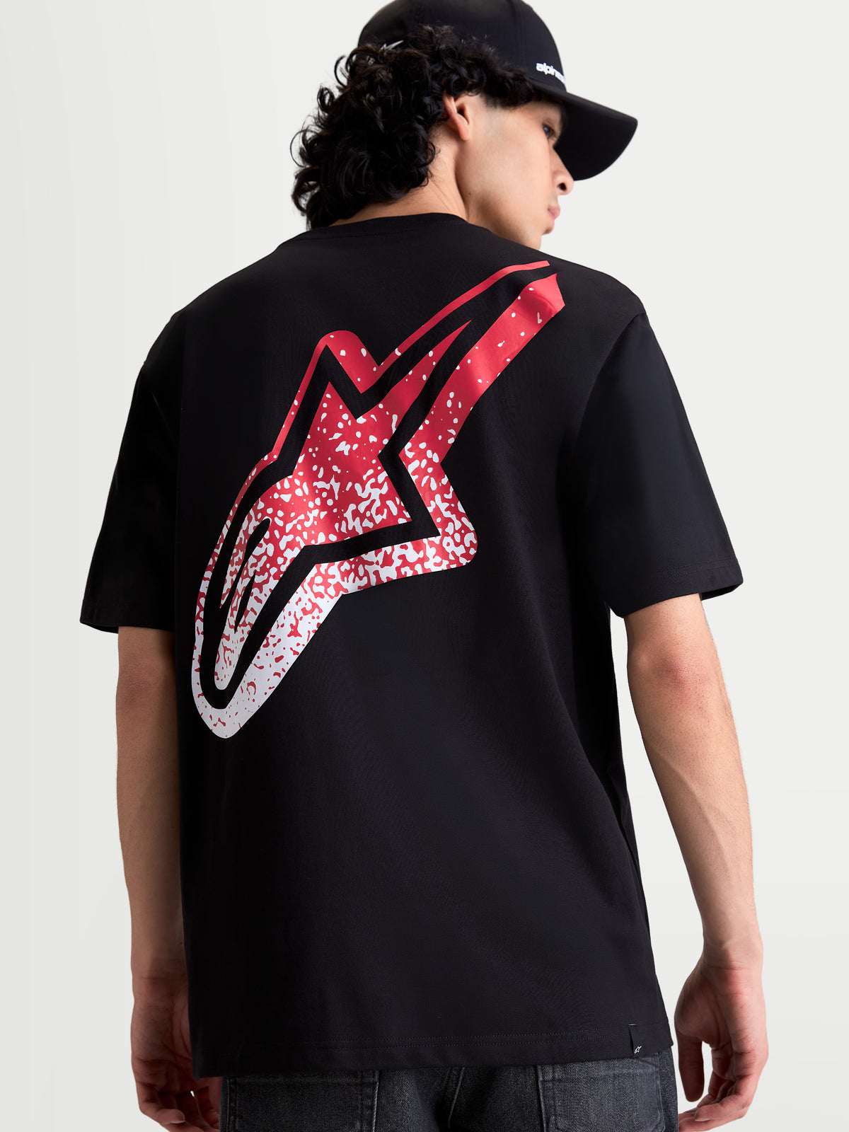 Alpinestars Meteor CSF T-shirt, svart kortärmad t-shirt sedd bakifrån på modell, stor röd och vit MX-inspirerad Astars-logotyp med färgtoning på ryggen, bekväm motorsportinspirerad sportswear.