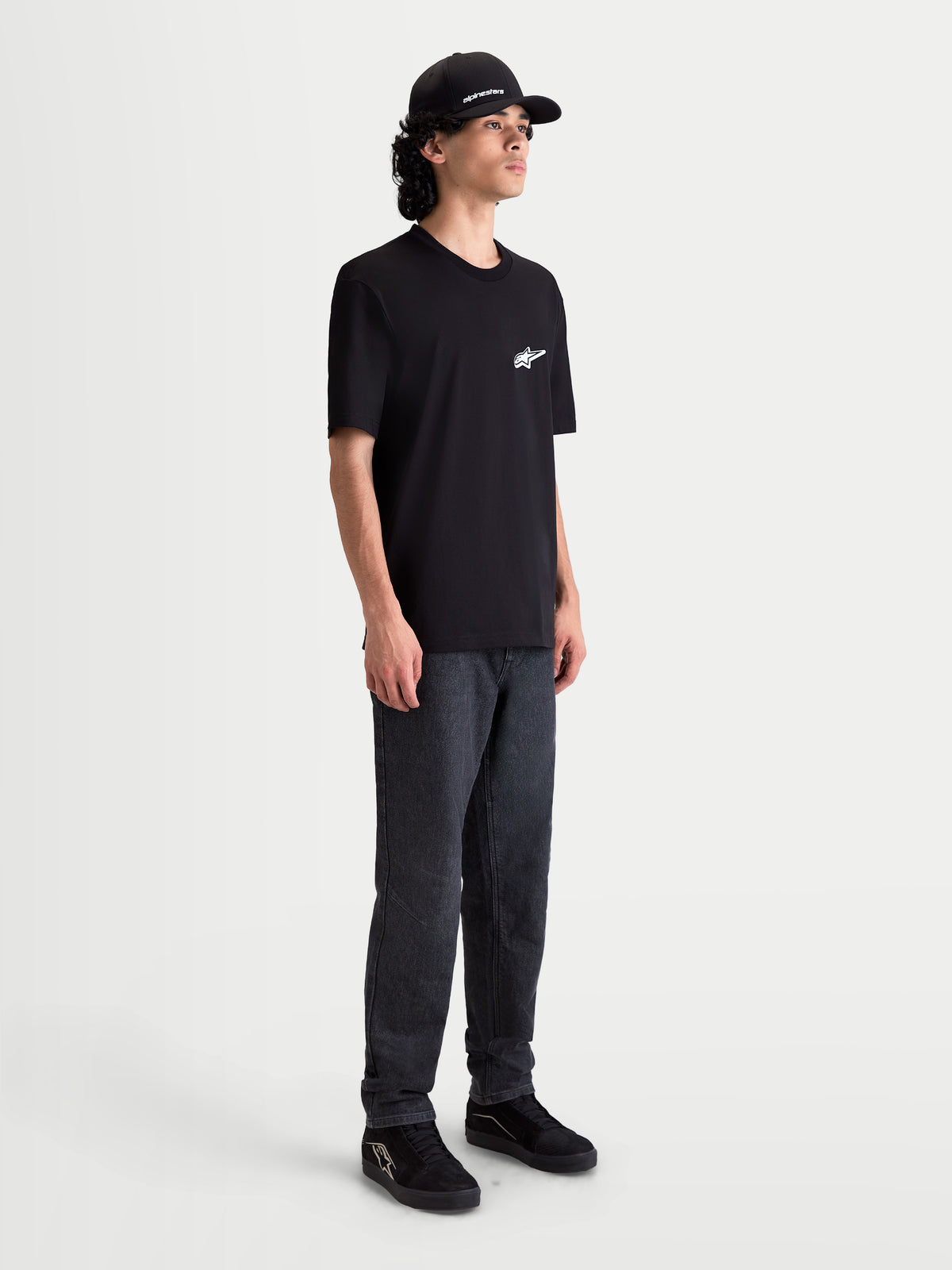 Alpinestars Meteor CSF t-shirt, kortärmad herrt-shirt, svart med vit MX-inspirerad logotyp på bröstet, bomull- och polyesterblandning, visas på en modell i en motorsport-inspirerad vardagsstil.