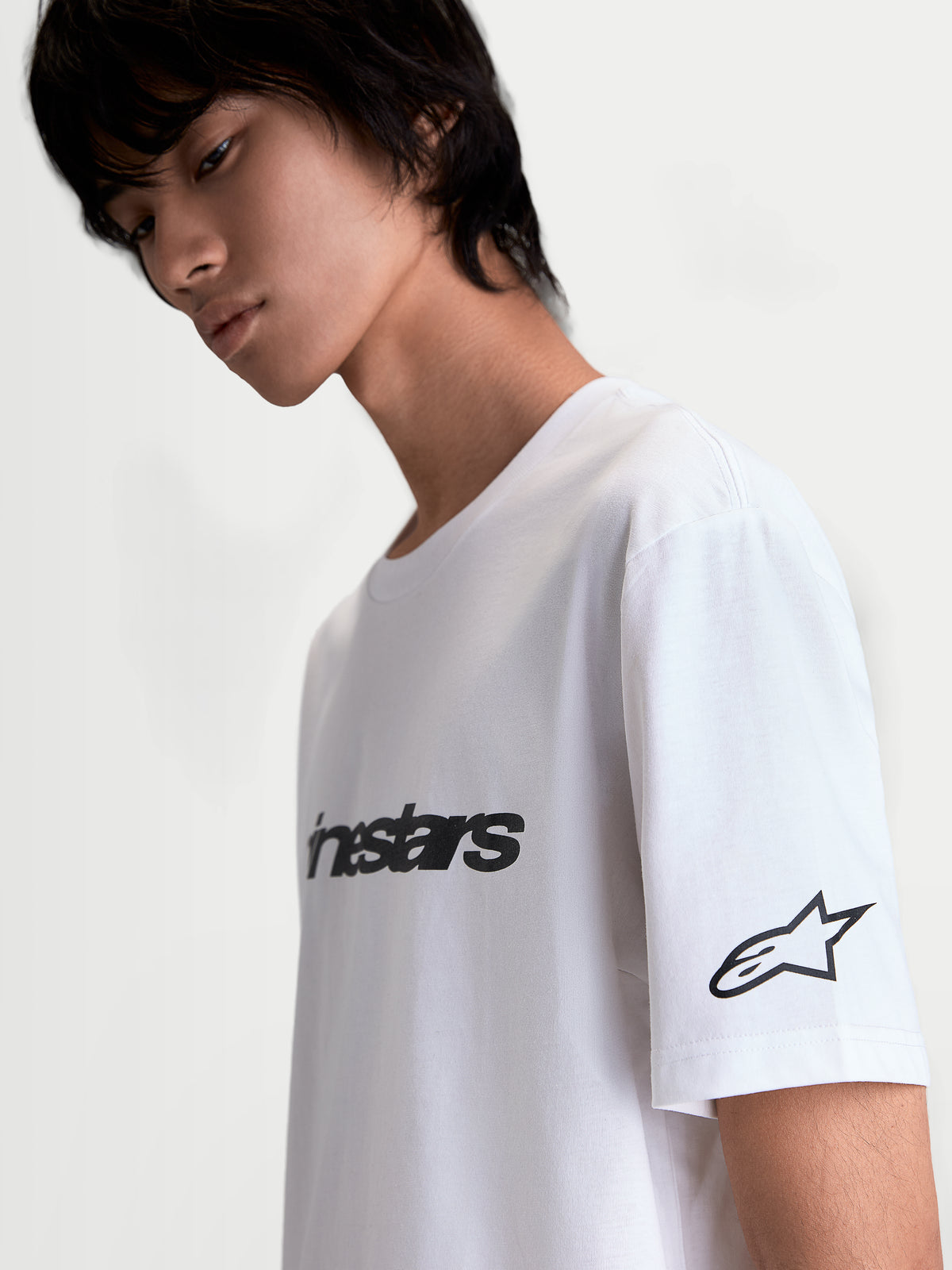 Alpinestars Race Wordmark CSF t-shirt, vit kortärmad t-shirt med svart ordmärke på bröstet och Ageless-stjärnlogotyp på ärmen, bekväm motorsport-streetwear i bomull-polyesterblandning, sedd från sidan på modell.