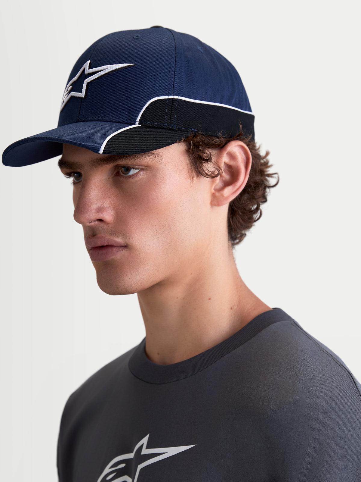 Alpinestars 500 Snapback keps, sportswear-keps för vardagsbruk, mörkblå och svart, slitstark bomullstwill med 3D-broderad Astars-logotyp och vit kontrasterande passpoal, böjd skärm, på modell i sidovy.