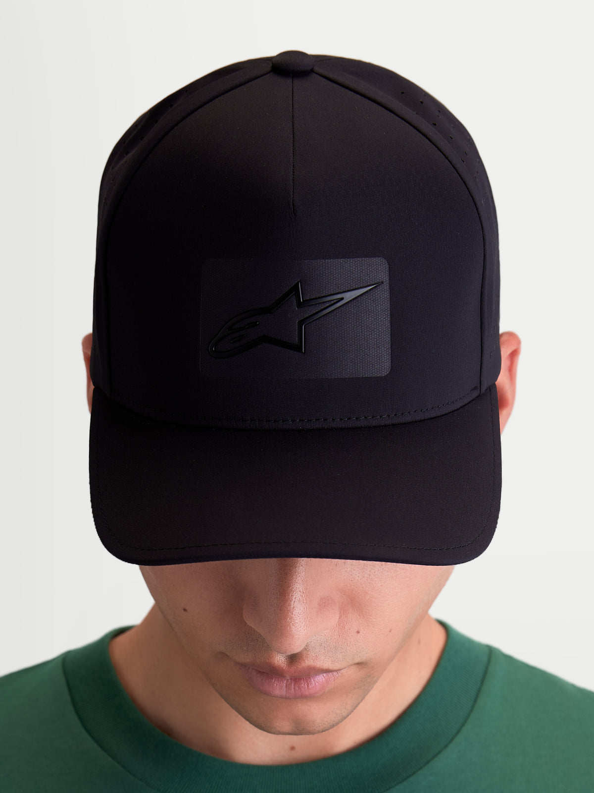 Alpinestars Algo Perf Ajustable keps, sportig keps i svart tekniskt tyg med sidoperforeringar för ventilation, böjd skärm och strukturerad krona, framifrån på modell med sonic-weldad Astars-logotyp.