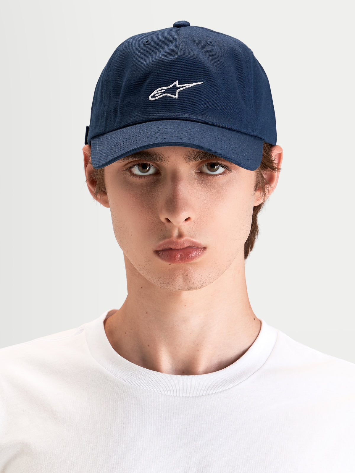 Alpinestars Dylan Dad Keps, marinblå keps med vit Astars-logobrodyr, böjd skärm och ostrukturerad låg krona, buren av en modell