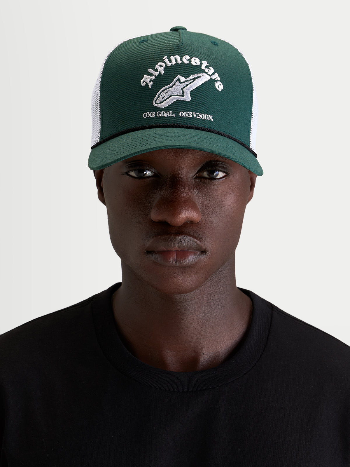 Alpinestars Baron Trucker keps, grön och vit vardagskeps med böjd skärm, strukturerad krona och meshbaksida, bärs av en modell