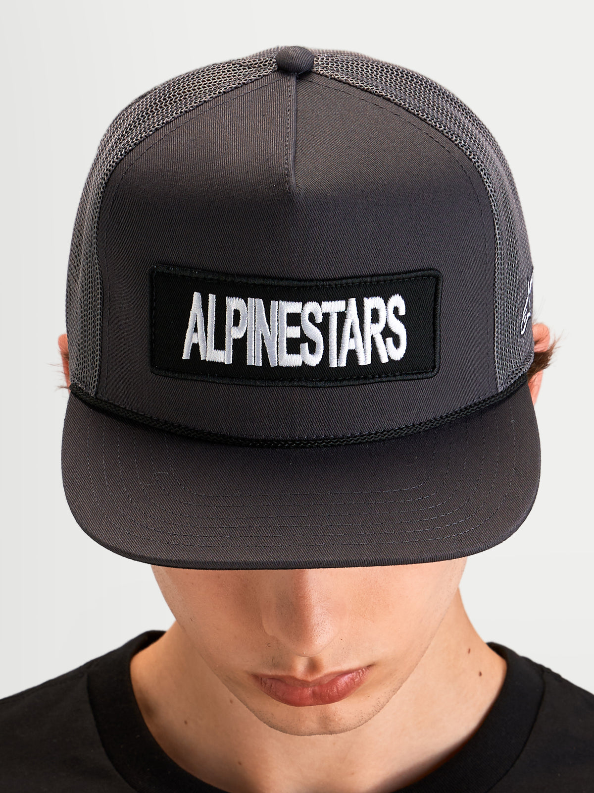 Alpinestars Ten keps, mörkgrå keps med platt skärm och strukturerad meshkrone, broderad logotyppatch framtill, bärs av en modell