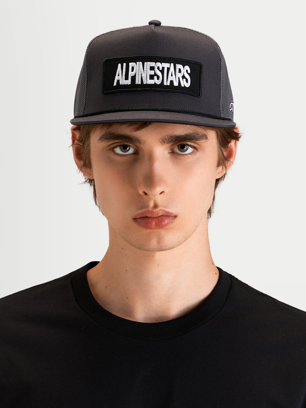Alpinestars Ten keps, mörkgrå keps med platt skärm och strukturerad krona, med broderad Alpinestars-ordlogopatch framtill, bärs av en modell