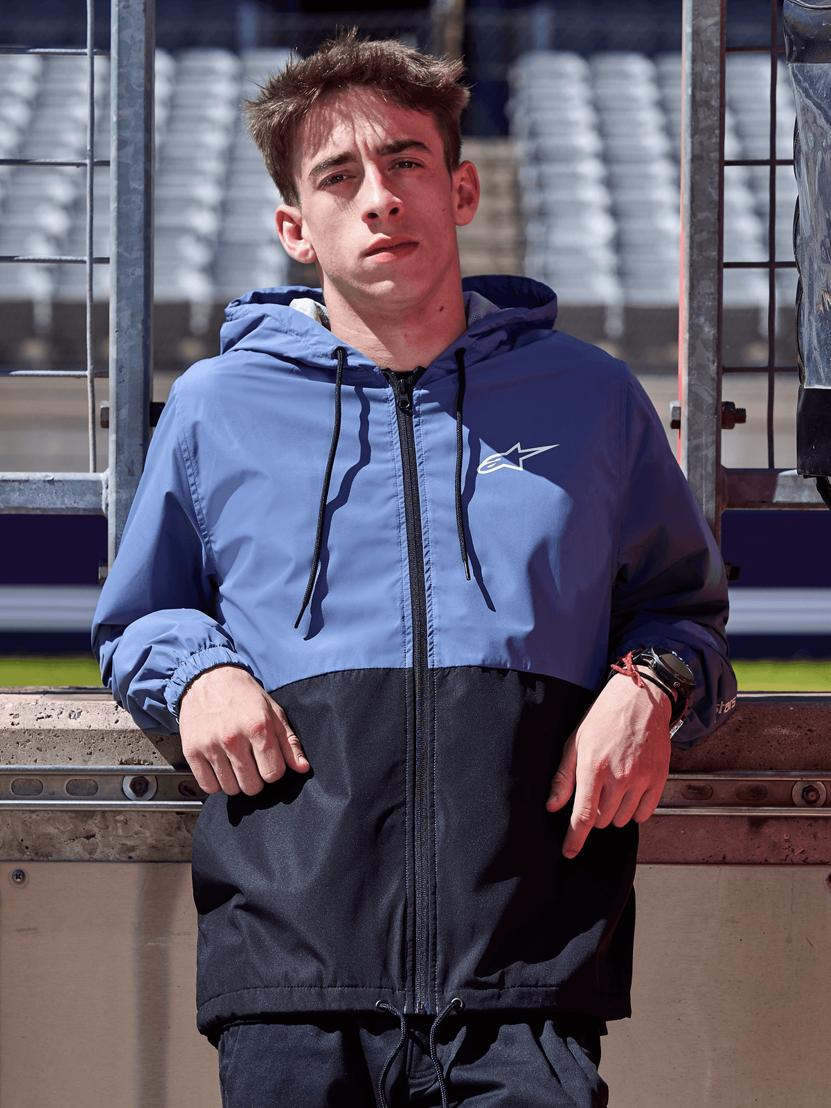 Alpinestars Speeder Windbreaker Jacket, Slate Blue and Black, hooded windbreaker with blocked body design, white logo on chest, casual lifestyle apparel worn at a racetrack