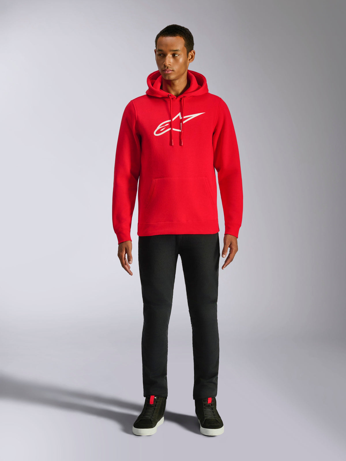 Alpinestars Ageless V3 Hoodie, casual streetwear, Red with white embroidered Alpinestars logo, worn by a male model with black pants, drawstring hood, front kangaroo pocket, modern motorsport-inspired design