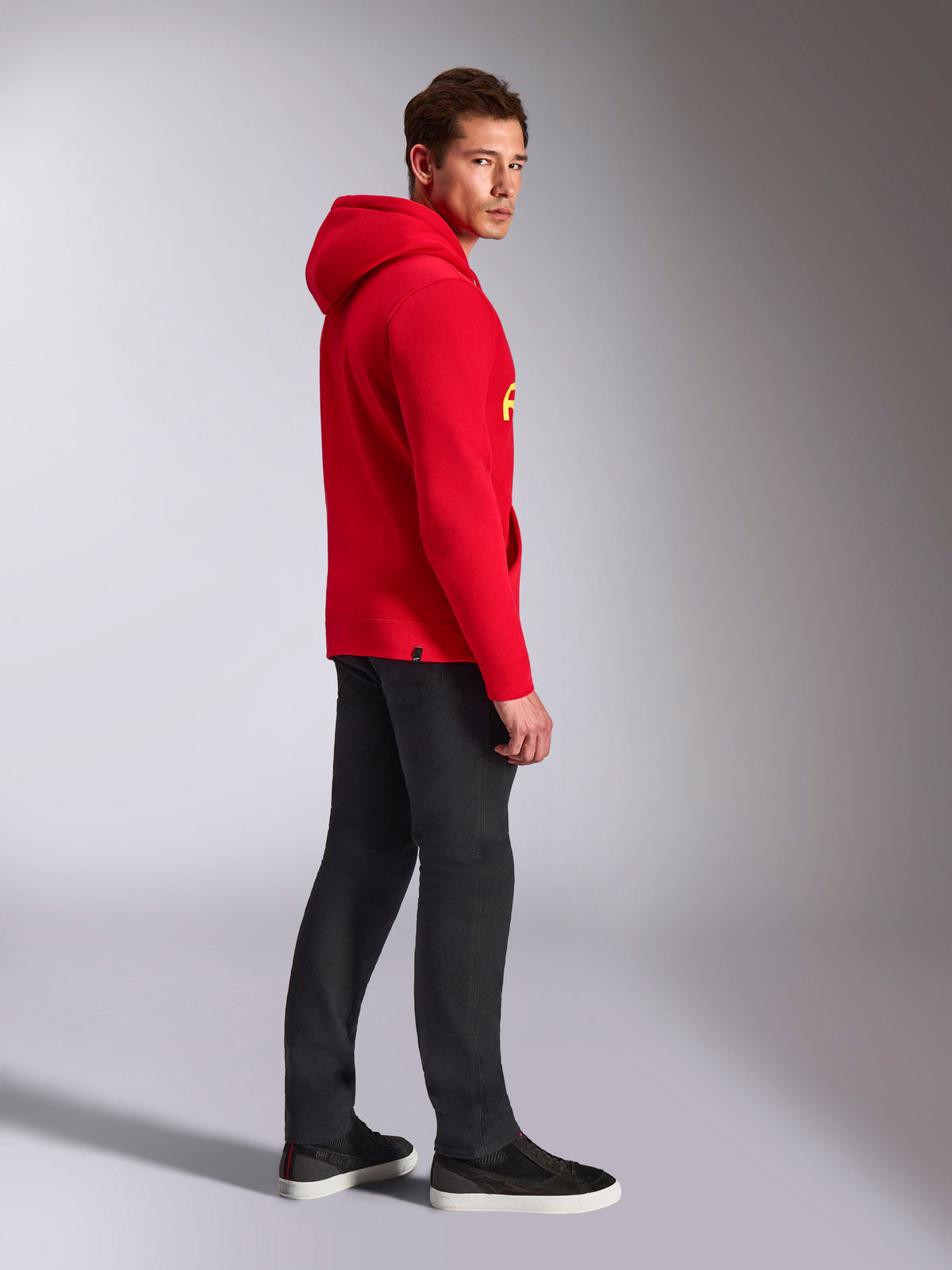 Alpinestars Ride V3 Hoodie, casual sportkläder, röd med Hi-Vis gul logotyp, manlig modell i röd huvtröja med svarta byxor och sneakers, sidoprofil, pullover-design i fleece med ribbade muddar och fåll.
