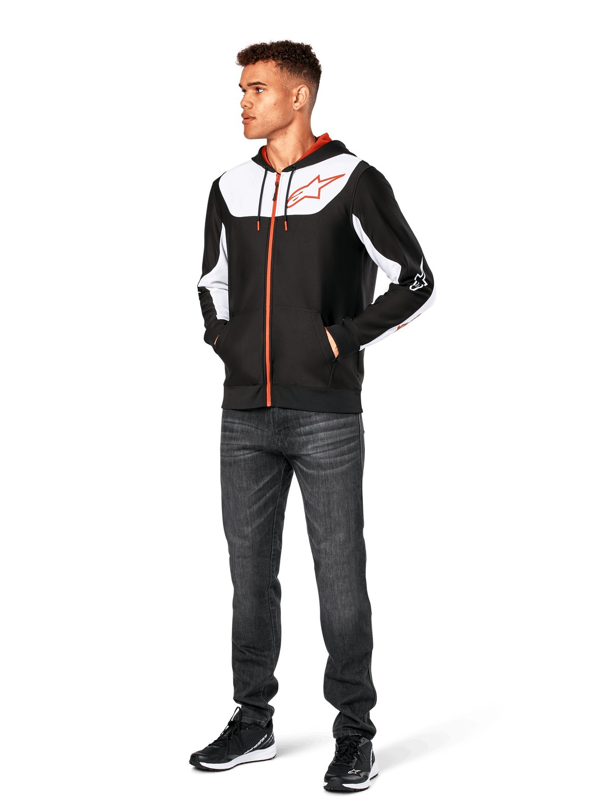 Alpinestars Sessions V3 Hoodie, vardaglig huvtröja med dragkedja fram, svart, vit och röd, bärs av en modell med mörka jeans och svarta sneakers, vita färgblockspaneler på bröstet och ärmarna, röda detaljer på dragkedja och dragsnören, stor bröstlogotyp, motorsportinspirerat streetwear i polyfleece