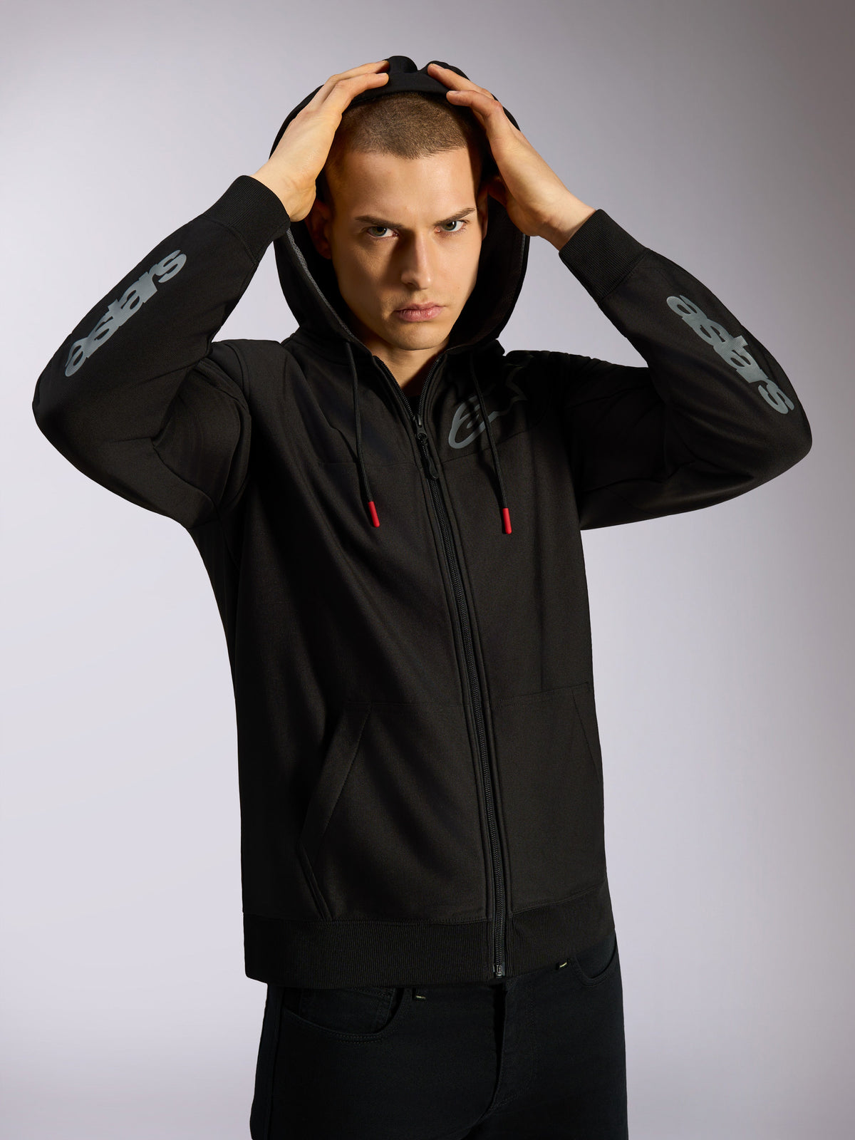 Alpinestars Sessions V3 Hoodie, svart huvtröja med hel dragkedja, grå Astars-logotyper på underarmarna, meshfodrad huva med dragsnören med röda ändar, avslappnad motorsportinspirerad streetwear