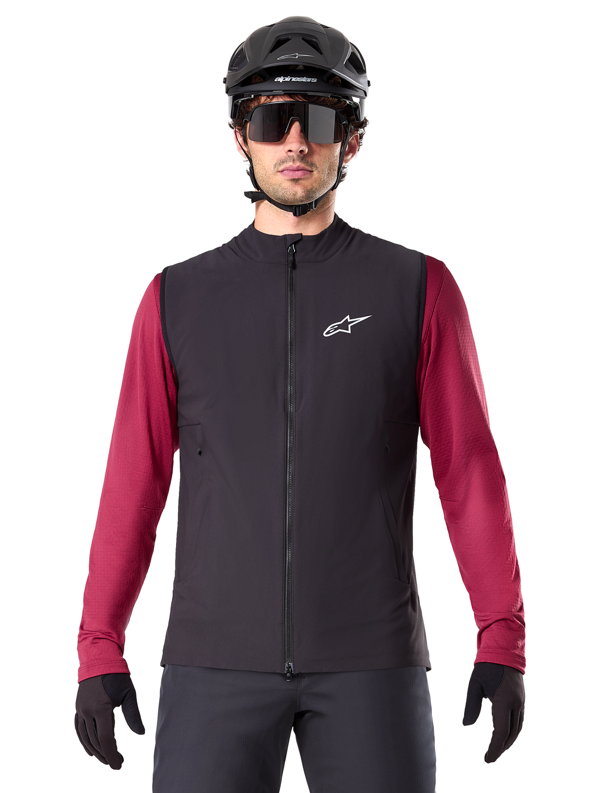 Alpinestars A-Dura Thermal Vest, Black insulated cycling vest, worn by a model with a maroon long-sleeve jersey, black MTB helmet, and sunglasses, featuring a white logo on the chest, lightweight thermal protection for mountain biking