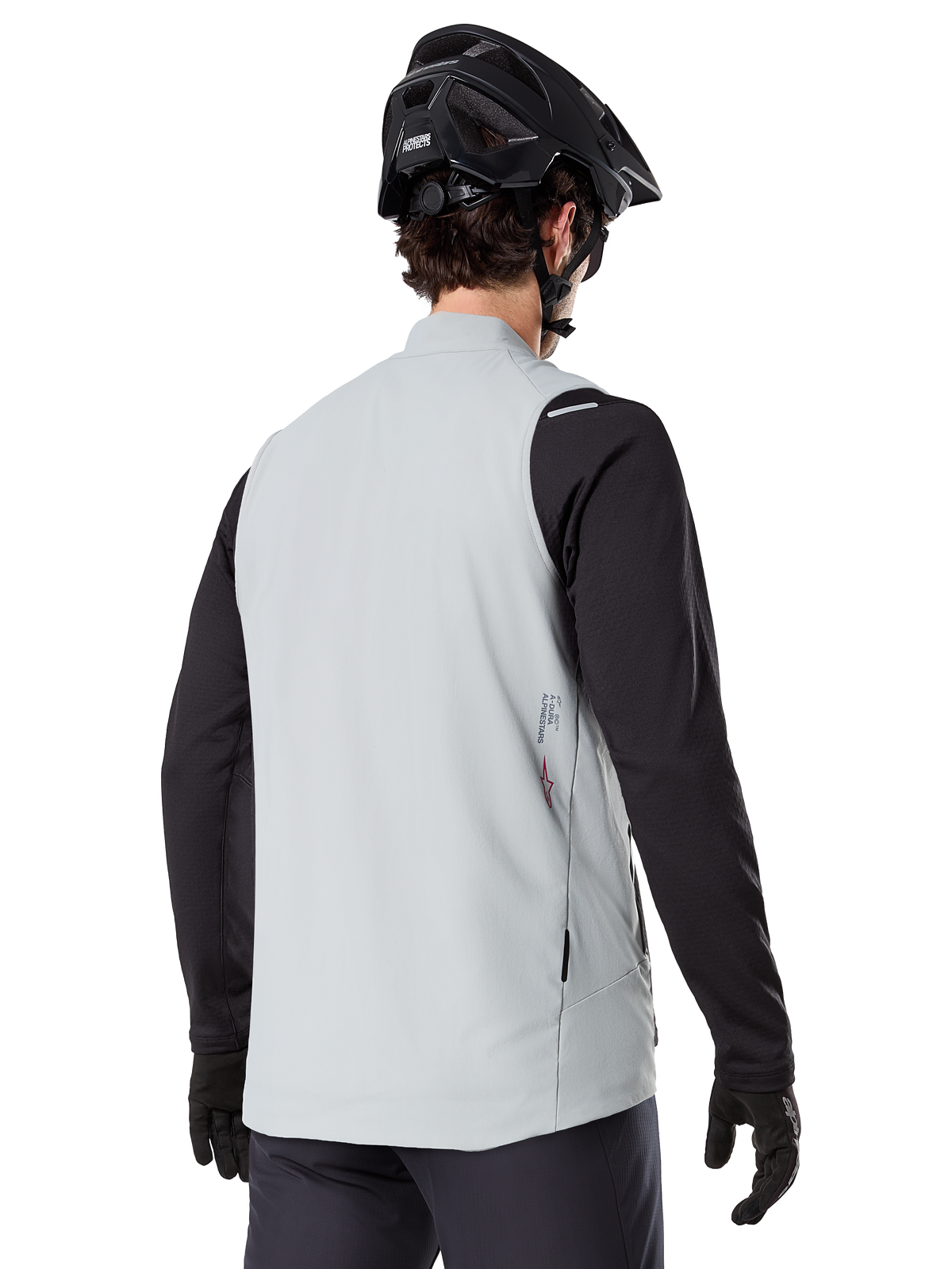Alpinestars A-Dura termisk väst, titaniumgrå, bakifrån av modell som bär en svart långärmad tröja och MTB-hjälm, minimalistisk design med liten röd stjärnlogotyp på ryggen, lättisolerad cykelväst för terrängkörning