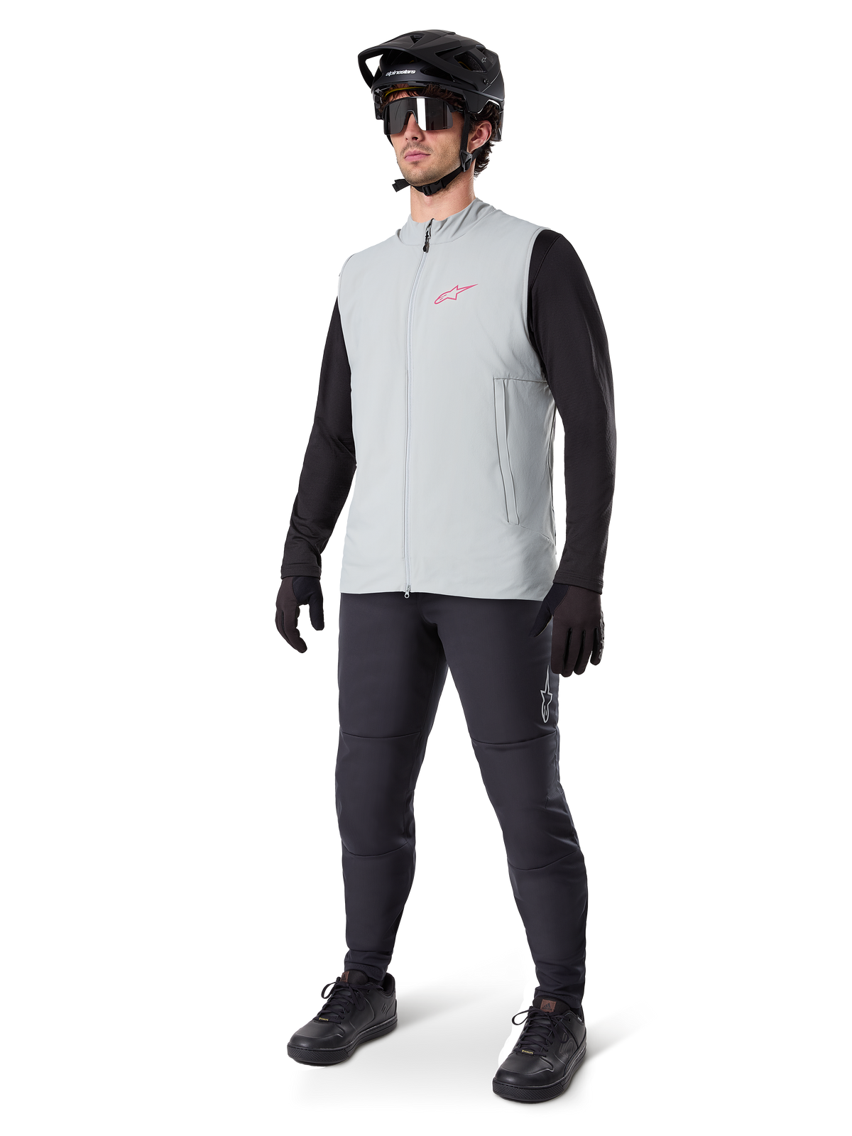 Alpinestars A-Dura Thermal Vest, titaniumgrå cykelväst med rosa logotyp, bärs av en modell med svart långärmad tröja, mörkgrå byxor och svart mountainbikehjälm, funktionsutrustning för cykling i kallt väder