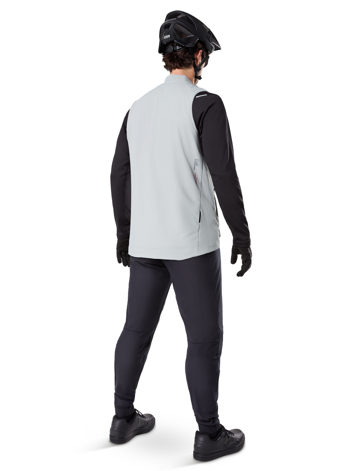 Alpinestars A-Dura Termisk Väst, Titanium Gray, ryggvy av modell som bär den isolerade cykelvästen över en svart långärmad tröja och mörka byxor, komplett med en svart mountainbikehjälm och handskar, designad för terrängkörning i kallt väder