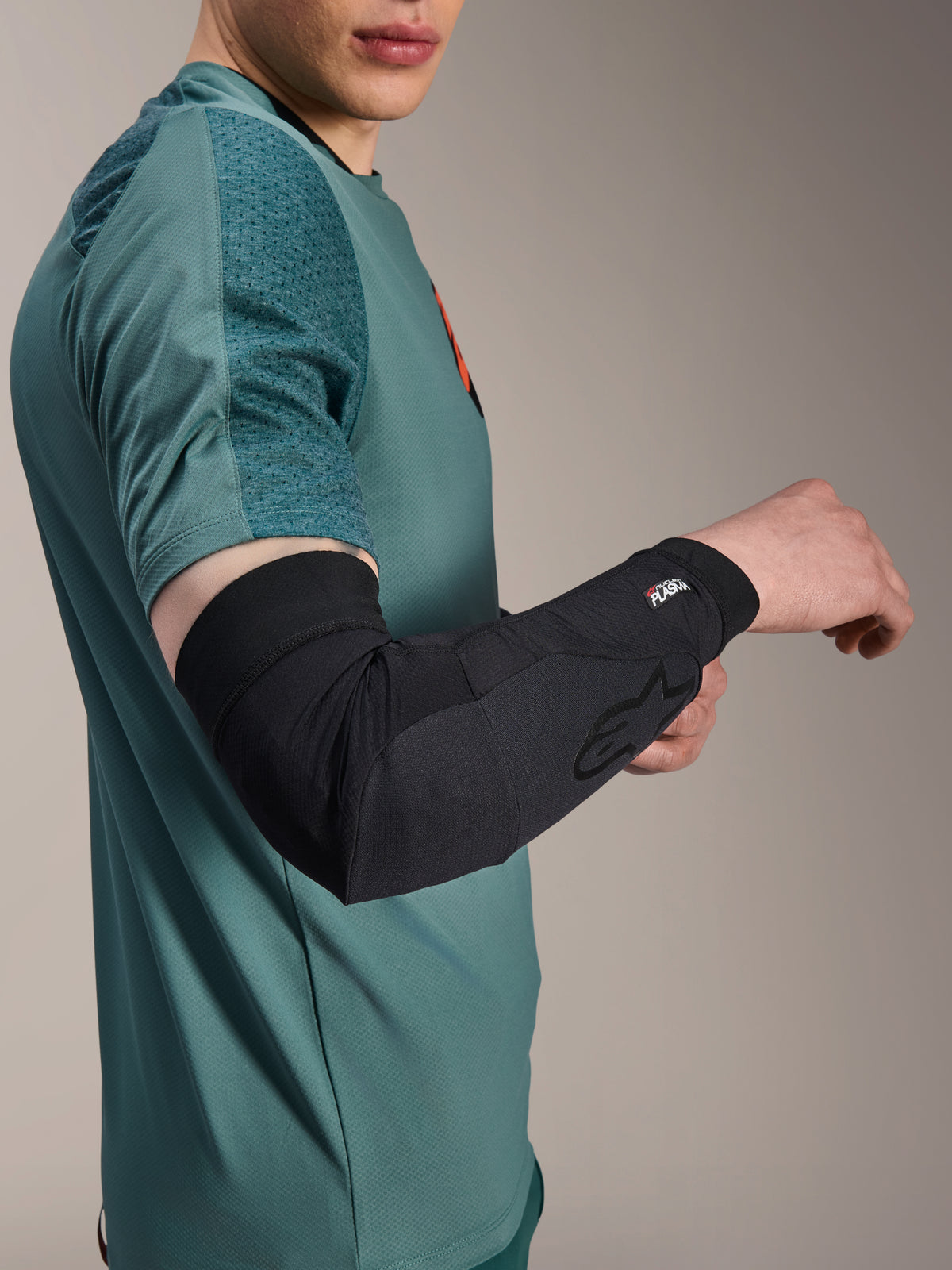 Alpinestars A-Motion Plasma armbågsskydd, svarta, bärs av en åkare i blågrön tröja, med Alpinestars-logotyp och Nucleon Plasma-märkning, smidig och ventilerande design för MTB-skydd