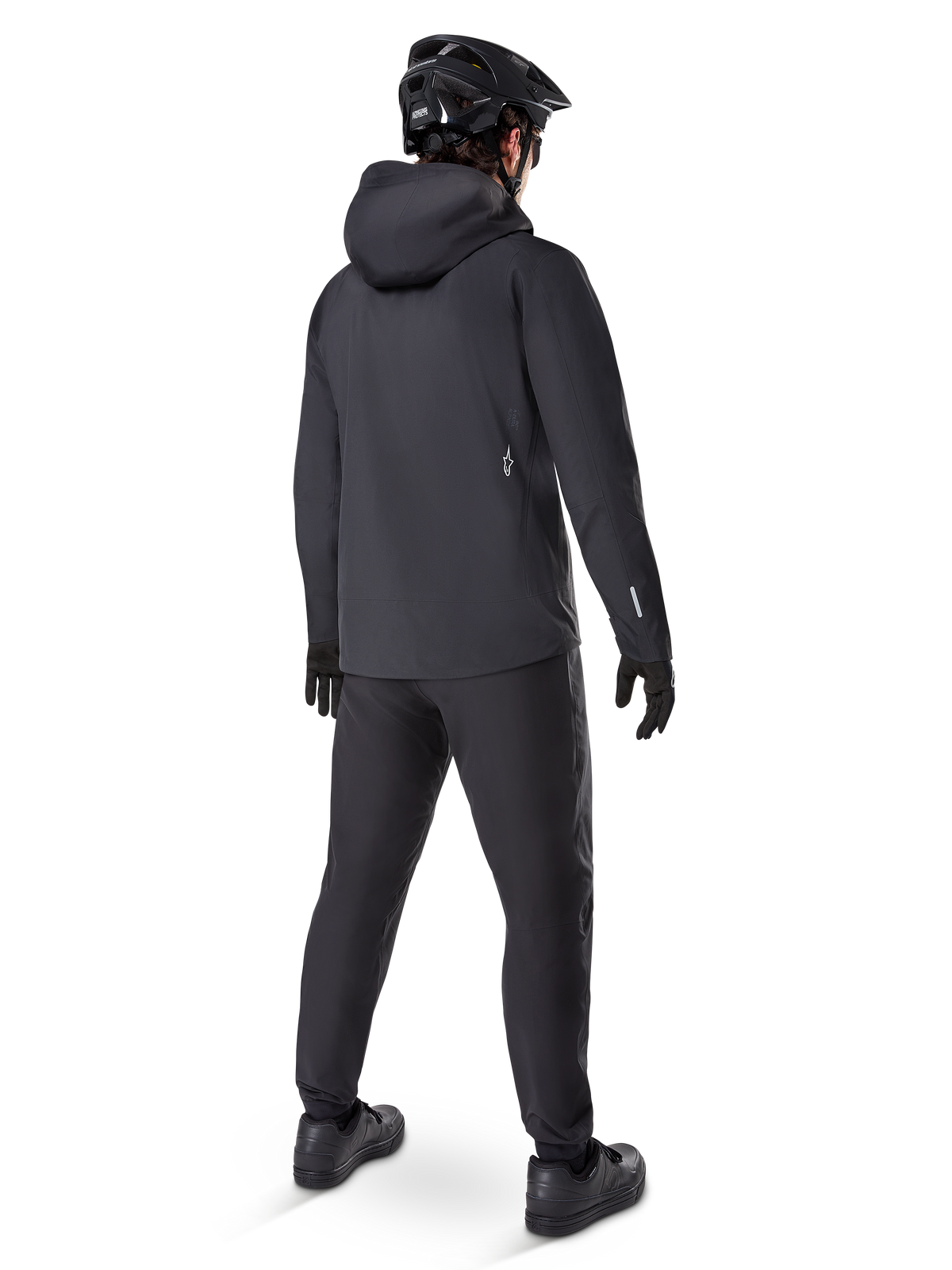 Alpinestars A-Dura Waterproof Pants, MTB-byxor, svarta, sedda bakifrån på en cyklist klädd i en helsvart mountainbike-utrustning inklusive huvjacka och hjälm, slitstark vattentät utrustning för leriga stigar