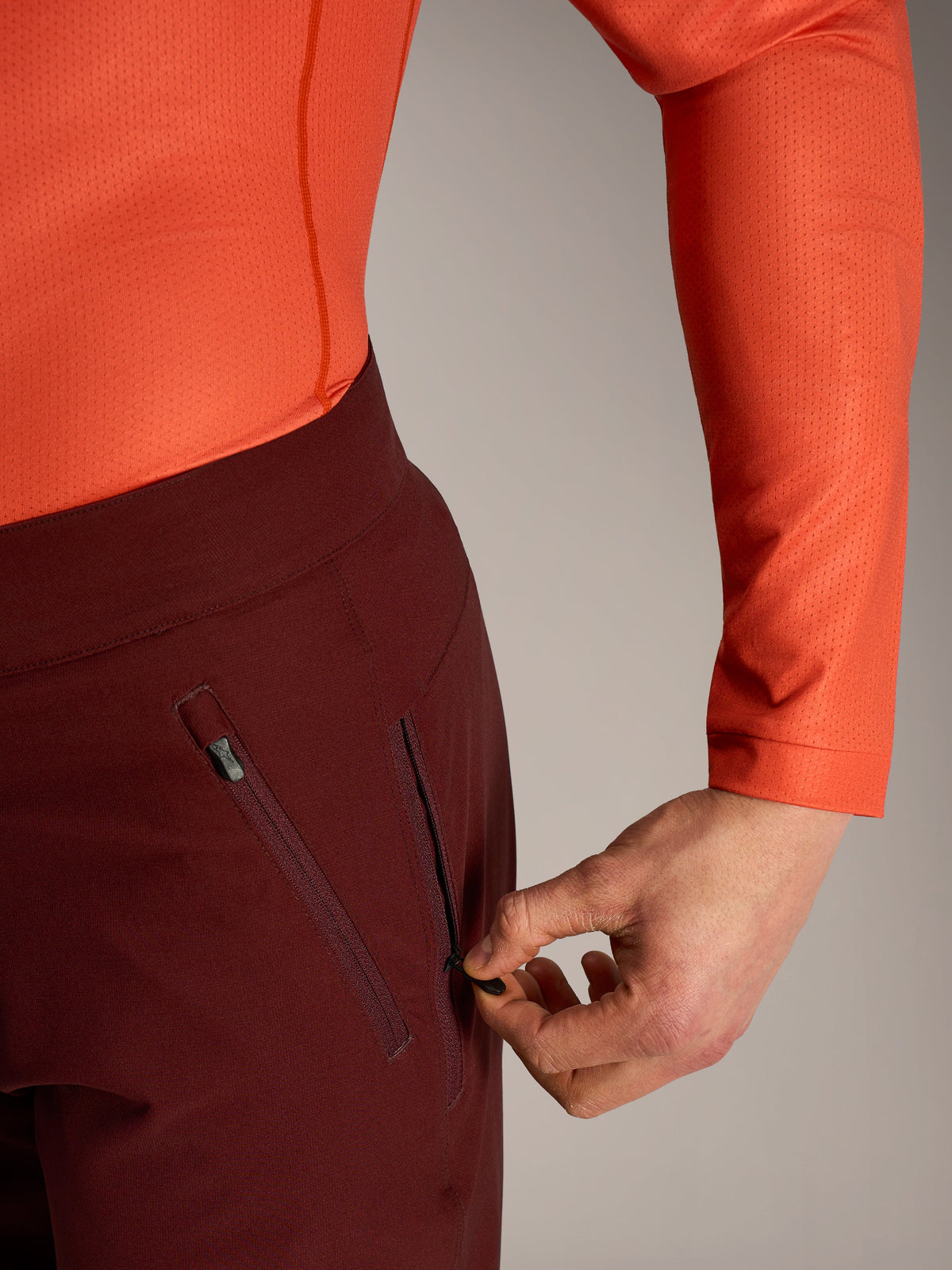 Alpinestars A-Dura Ride Shorts i bordeaux, närbild på hand som öppnar den säkra sidofickan med dragkedja.