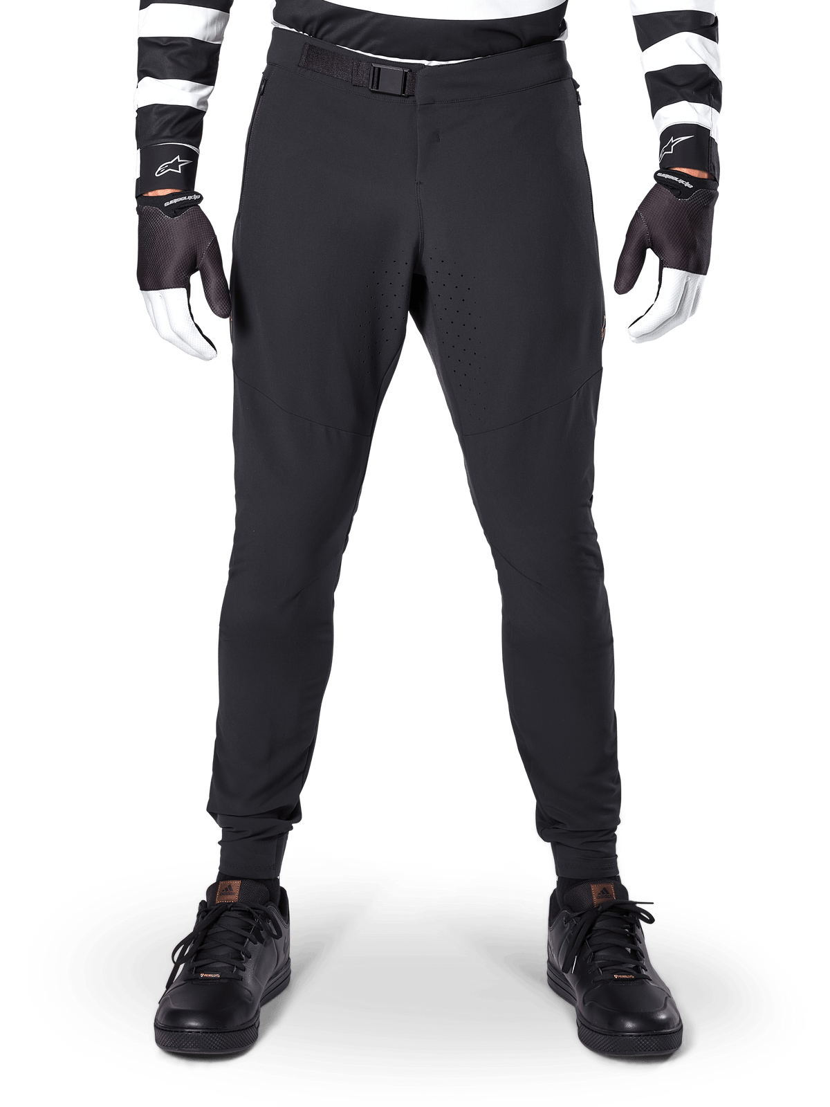 Alpinestars A-Aria Elite byxor, MTB-byxor, svarta, vy framifrån som visar laserperforeringar och magnetiskt spänne, bärs med en svartvitrandig tröja och svarta handskar, teknisk cykelutrustning för stigcykling