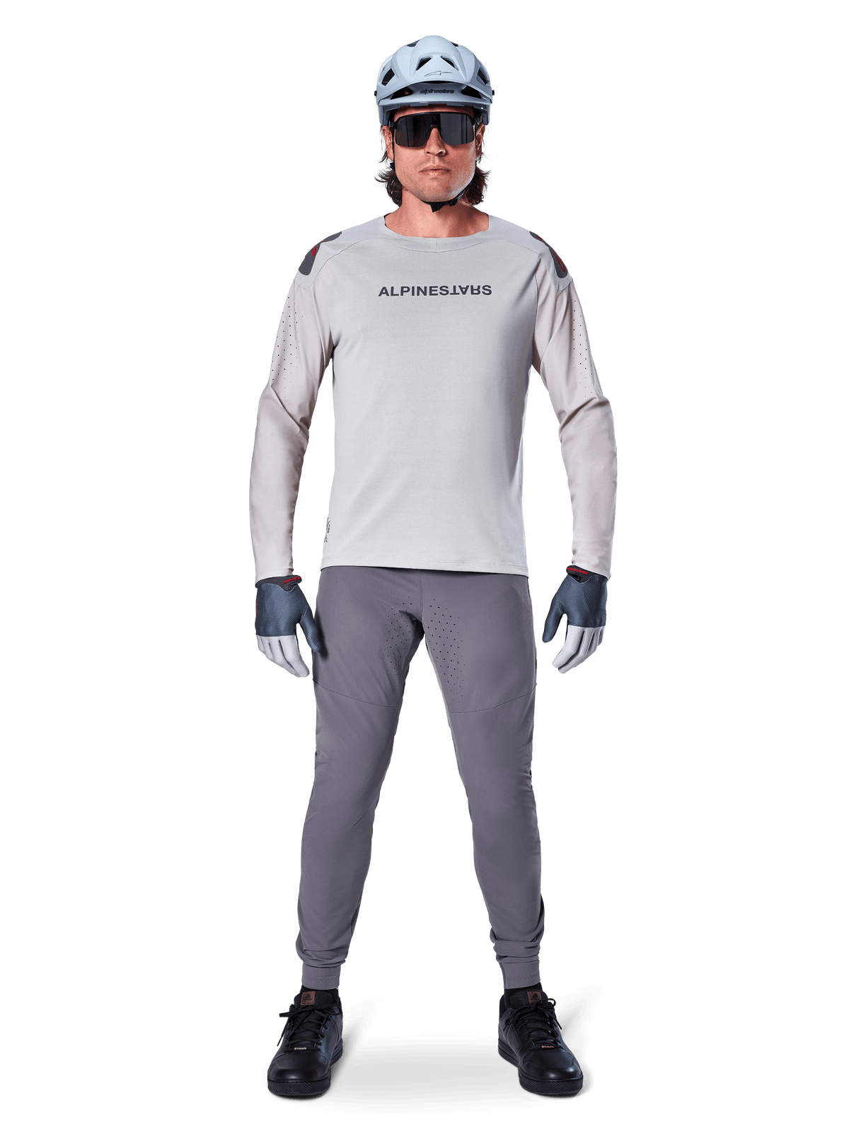 Alpinestars A-Aria Elite byxor, mörkgrå mountainbike-byxor, bärs av en cyklist i en ljusgrå långärmad tröja, ljusblå hjälm och svarta skor, med synliga laserperforeringar på innerbenen och en slimmad prestandapassform.