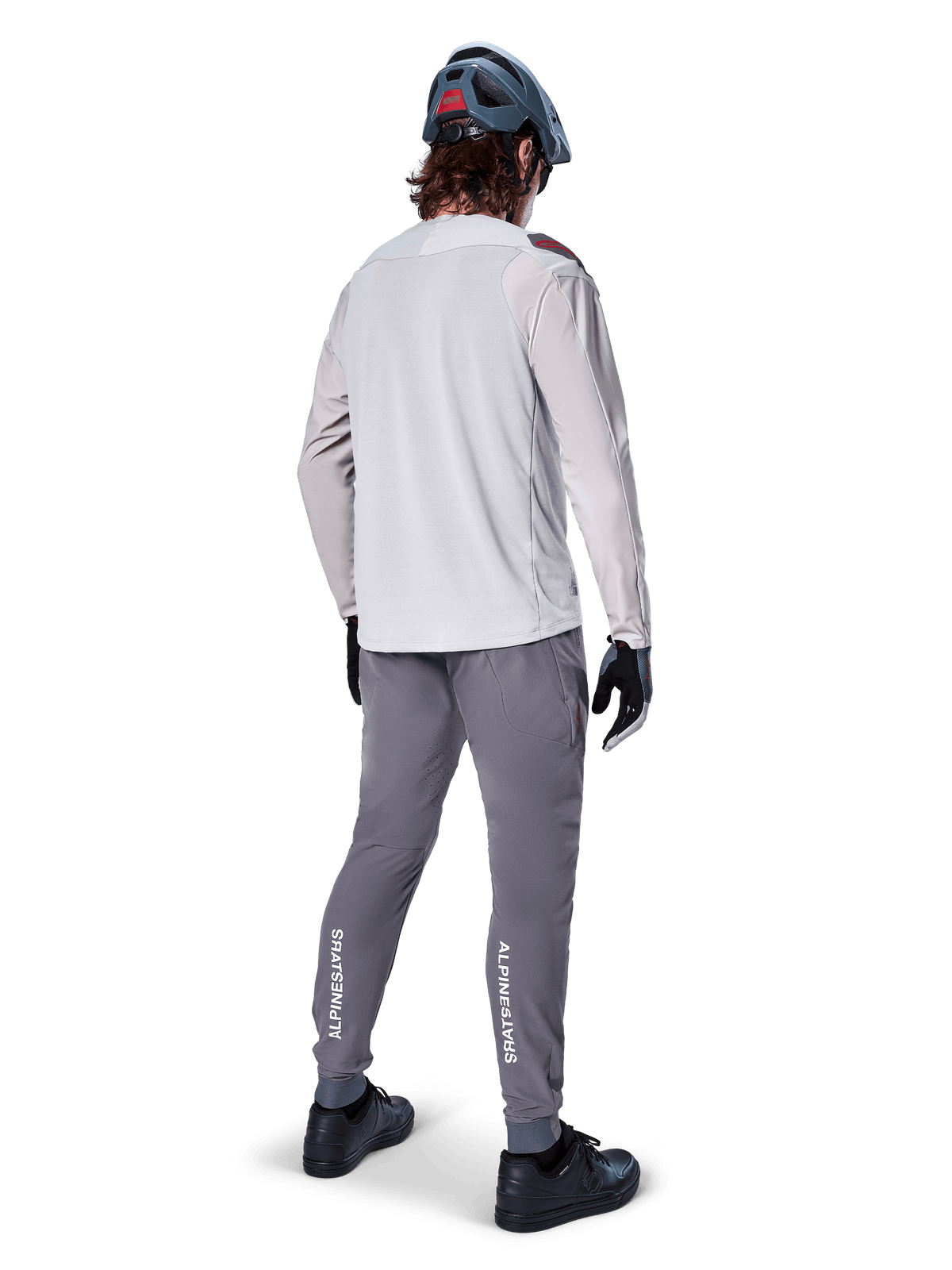 Alpinestars A-Aria Elite-byxor, MTB-byxor, mörkgrå, vy bakifrån av en cyklist i en hel outfit, vit Alpinestars-logotyp på underbenen, prestandapassform med laserperforeringar, matchad med en ljusgrå långärmad tröja och grå MTB-hjälm