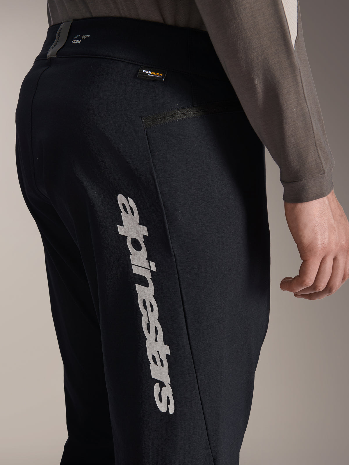 Alpinestars A-Dura Elite-byxor, svarta mountainbikebyxor, sidovy med stor vertikal Alpinestars-logotyp på benet, Cordura-etikett och sidoficka med dragkedja, teknisk cykelutrustning för terrängkörning
