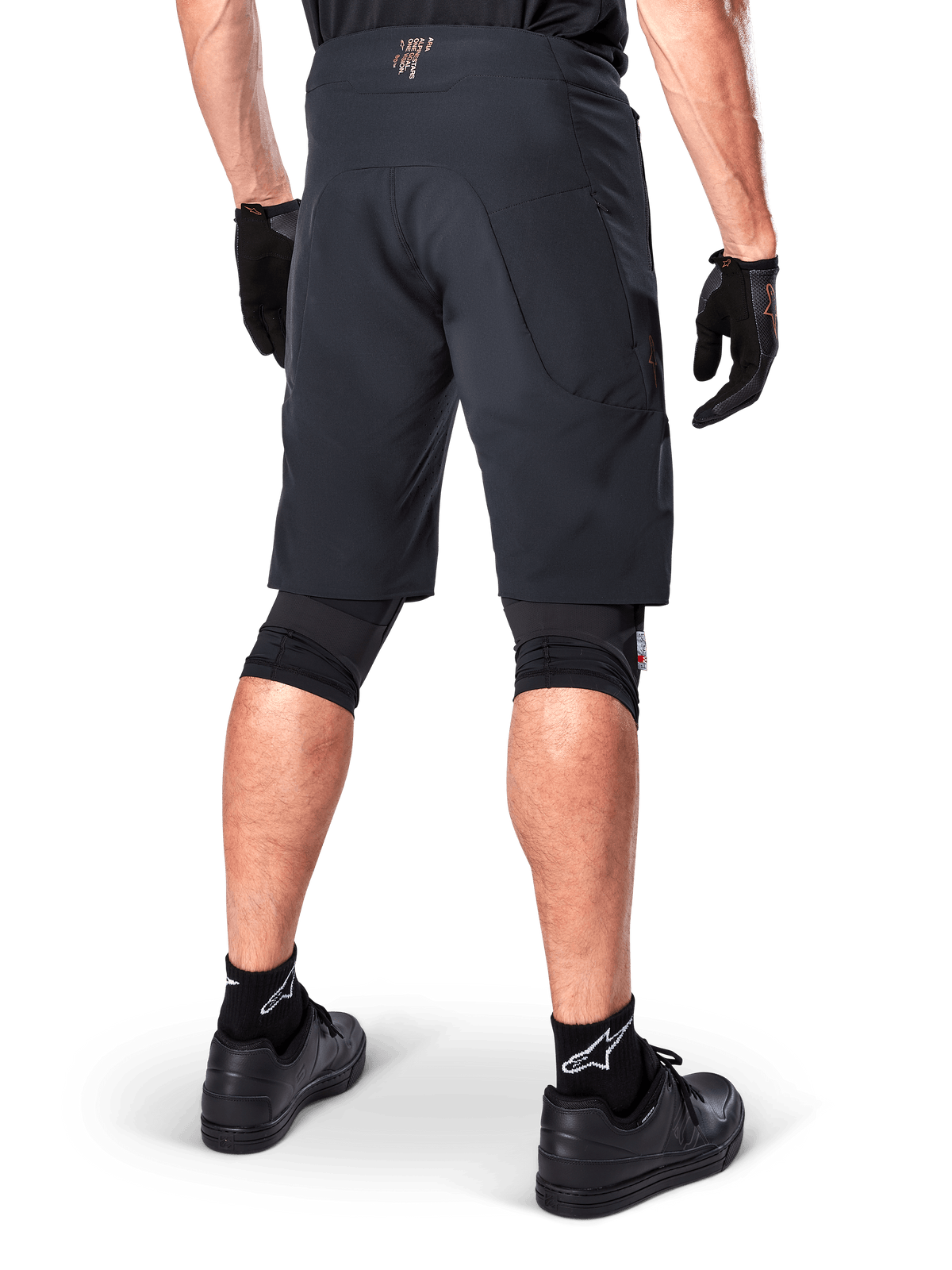 Vy bakifrån av en cyklist klädd i Alpinestars A-Aria Elite Shorts i svart, funktionella mountainbike-shorts, matchade med svarta cykelhandskar och svarta skor, designade för flexibel rörelse på terrängstigar