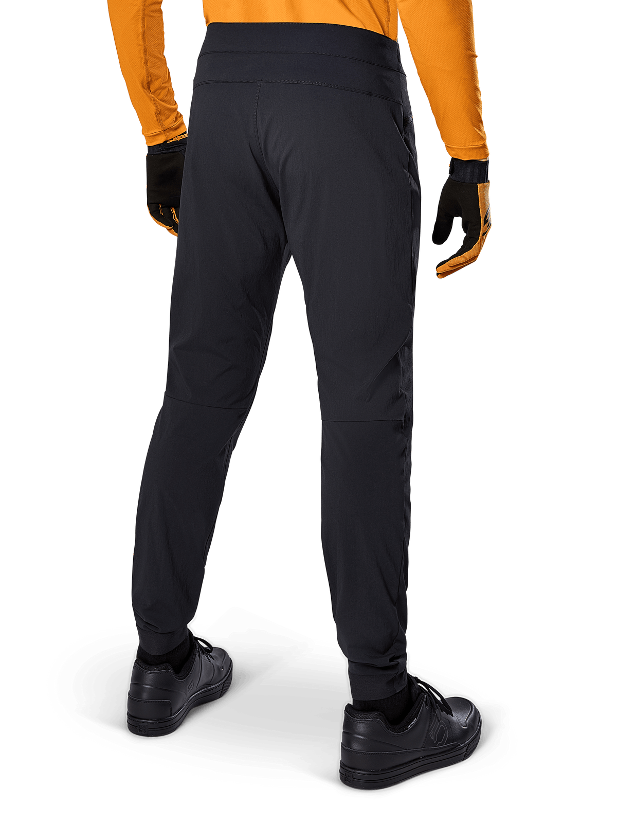 Alpinestars A-Dura-byxor, svarta MTB-byxor, sedda bakifrån, bärs med en orange långärmad tröja och svarta handskar, med elastiska muddar och slitstarkt textilmaterial för mountainbike