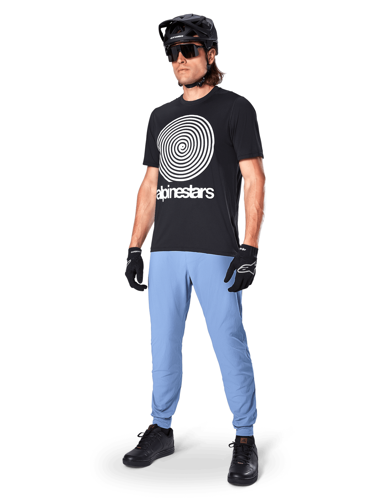 Alpinestars A-Dura byxor, MTB-byxor, Infinity Blue, bärs med svart grafisk t-shirt med vit spirallogotyp, svart hjälm, solglasögon och svarta handskar, professionell mountainbikeutrustning