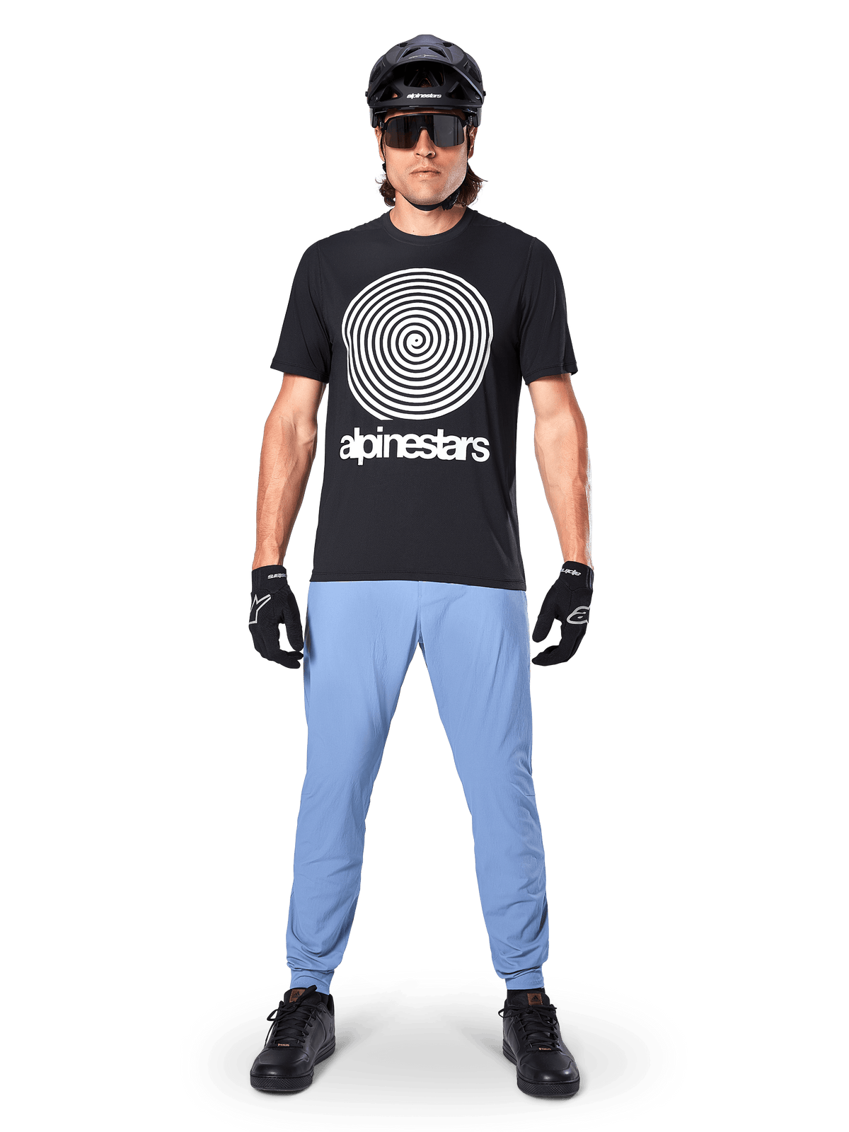 Alpinestars A-Dura byxor, Infinity Blue, MTB-byxor som bärs med en svart t-shirt med spiralgrafik, svarta handskar och en svart hjälm, med ett slitstarkt stretchmaterial och elastiska muddar, prestandautrustning för mountainbike