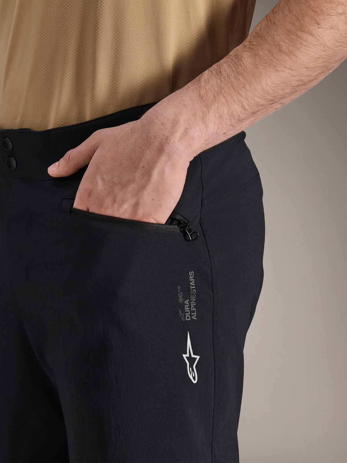 Alpinestars A-Dura Shorts, svarta mountainbike-shorts, närbild på sidoficka med dragkedja och en hand i fickan, med vit Alpinestars-logotyp och A-Dura-branding, slitstarkt material för terrängcykling
