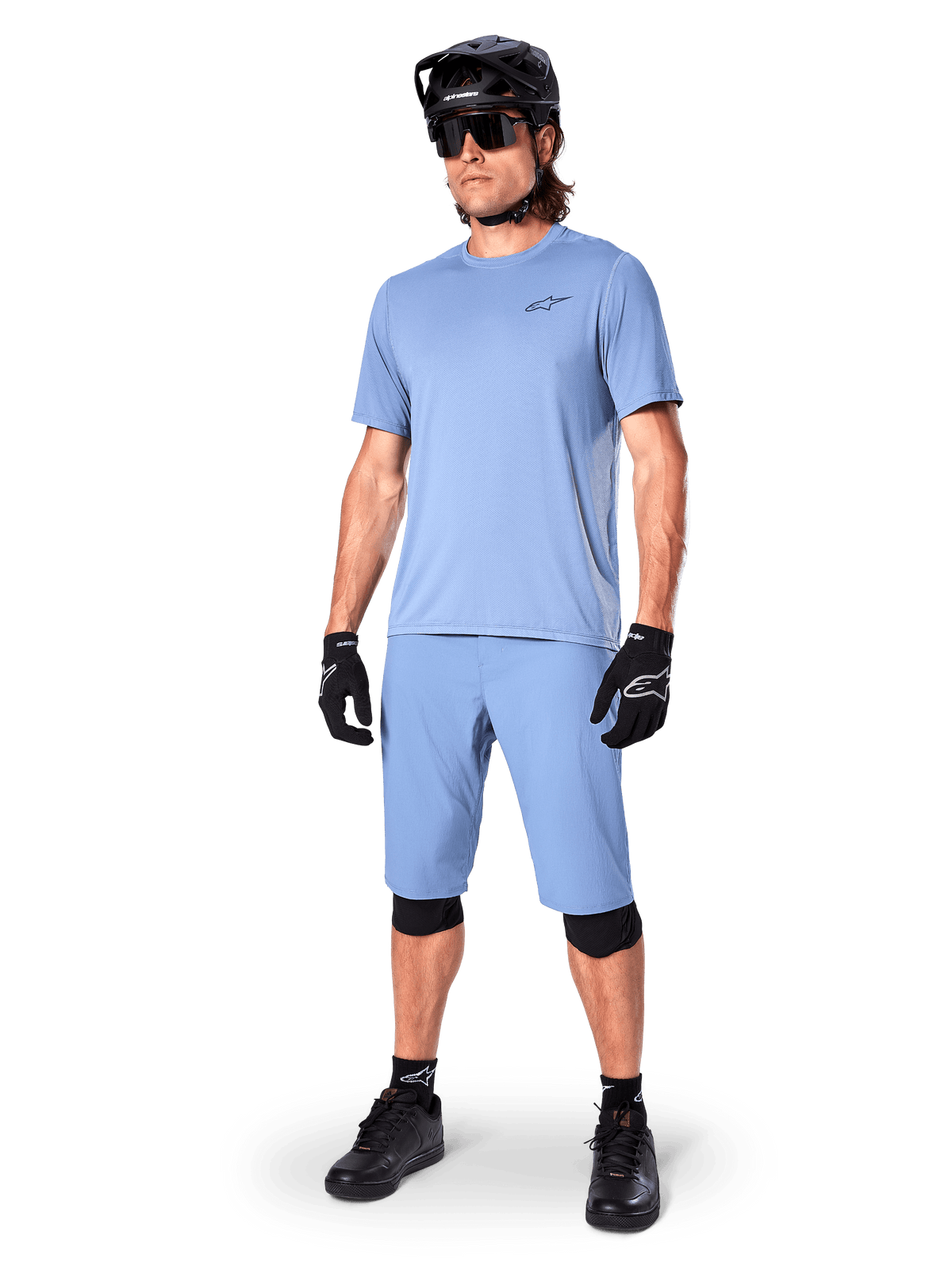 Modell klädd i Alpinestars A-Dura Shorts i Infinity Blue, matchande ljusblå kortärmad tröja, svart MTB-hjälm, solglasögon och svarta handskar, komplett mountainbike-outfit för stigcykling