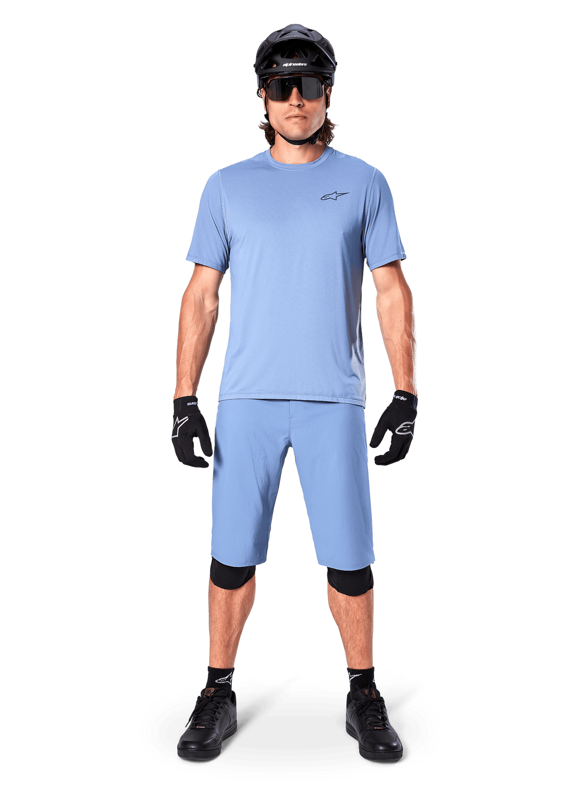 Modell som bär Alpinestars A-Dura Shorts i Infinity Blue, matchande ljusblå tröja, svart mountainbikehjälm, svarta solglasögon, svarta handskar och knäskydd, komplett MTB-outfit för trailcykling
