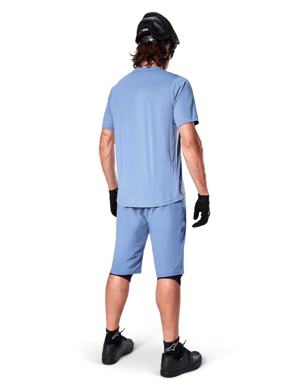 Vy bakifrån av en mountainbikecyklist iklädd Alpinestars A-Dura Shorts i Infinity Blue, matchande kortärmad tröja, svart hjälm, svarta handskar och svarta skor, koordinerad funktionsutrustning för MTB-trailcykling