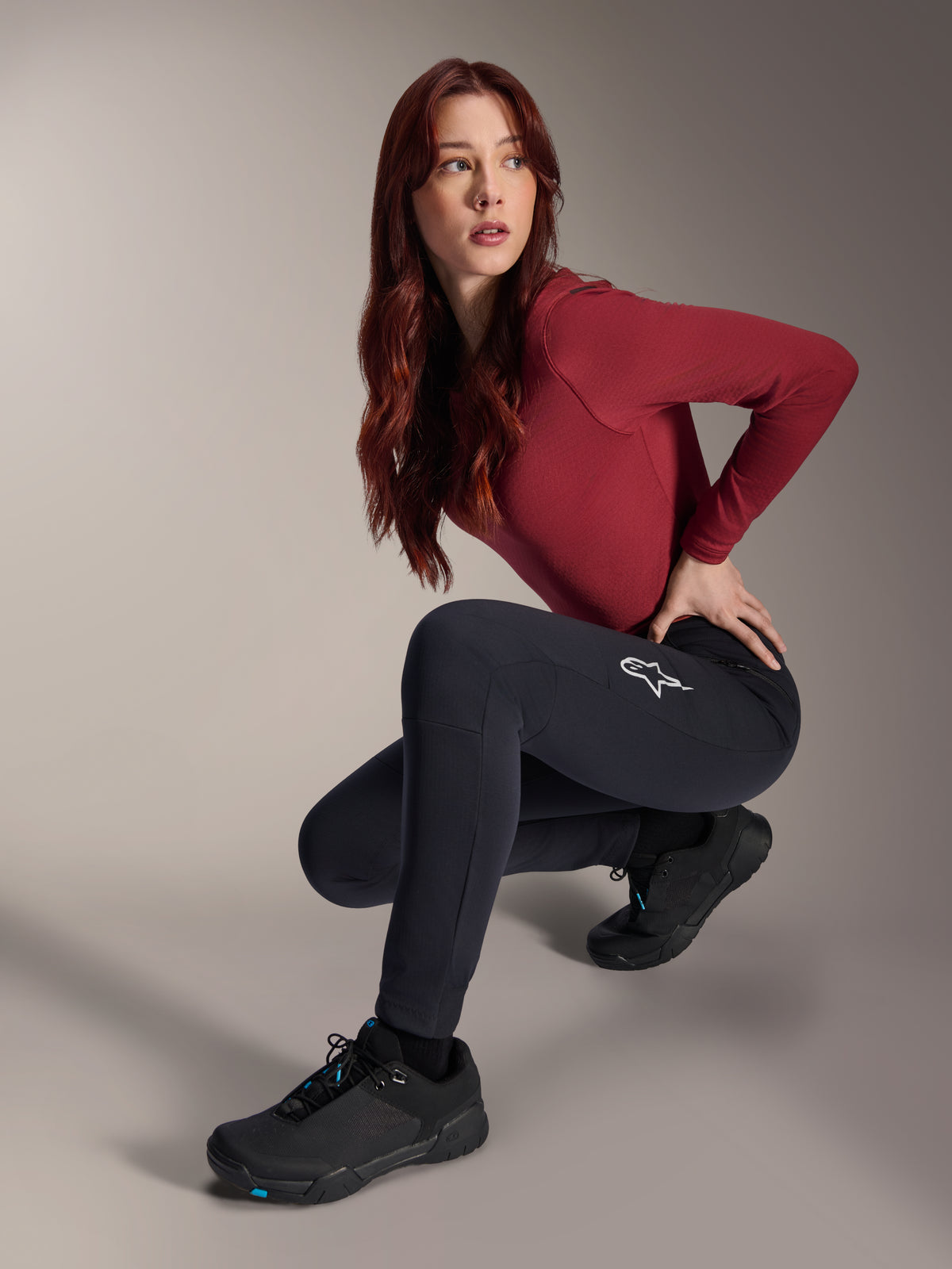Alpinestars Stella A-Dura Thermal Pants, MTB-byxor för damer, svarta, bärs av en modell i en hukande pose med en vinröd långärmad tröja och svarta cykelskor, vit stjärnlogotyp på låret, slitstark och varm konstruktion för terrängkörning i kallt väder