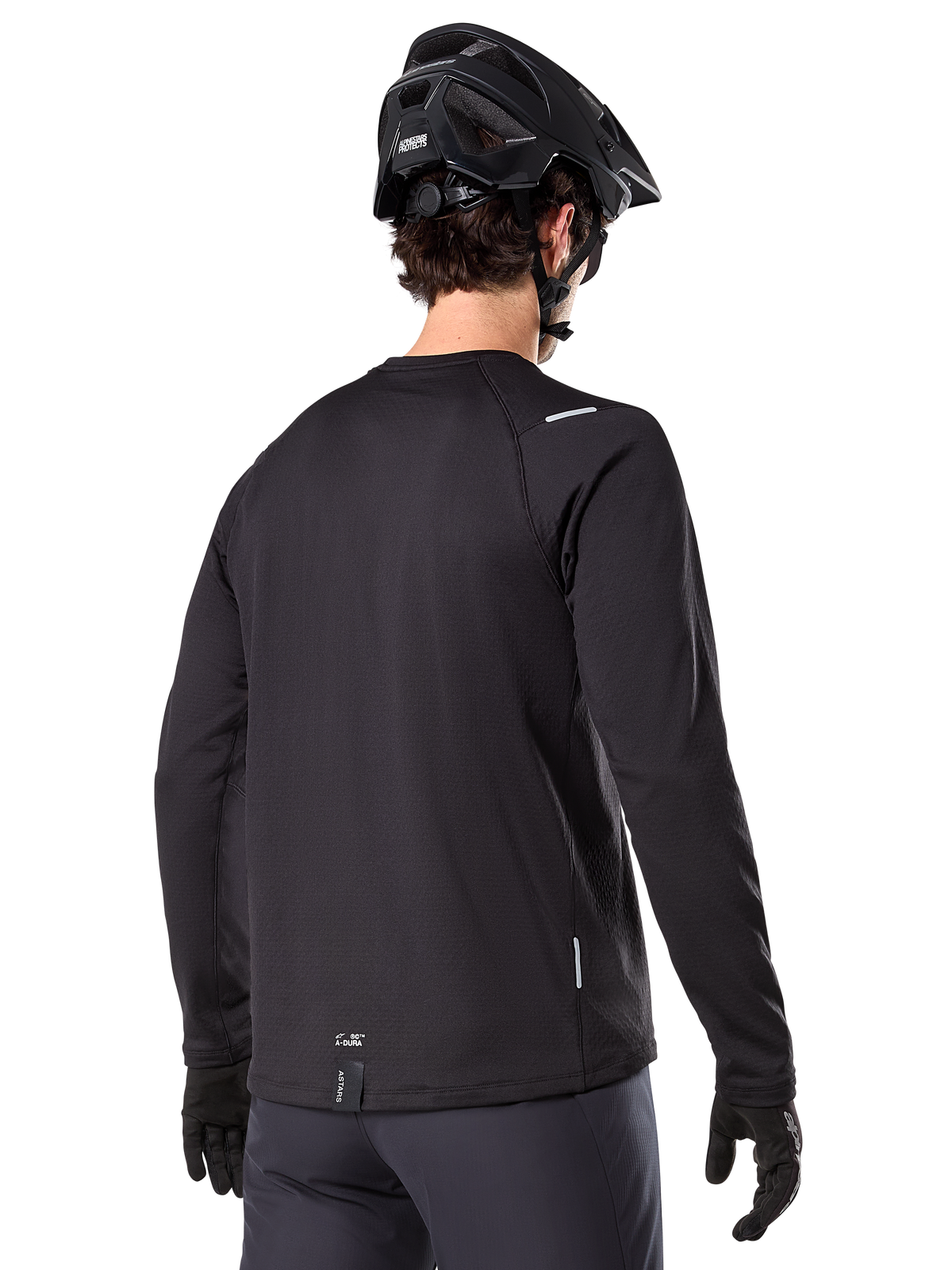 Alpinestars A-Dura Thermal Jersey, long-sleeve mountain bike jersey, Black, back view showing extended drop tail, small reflective details, and hem branding, worn with a black helmet and gloves for cold-weather cycling