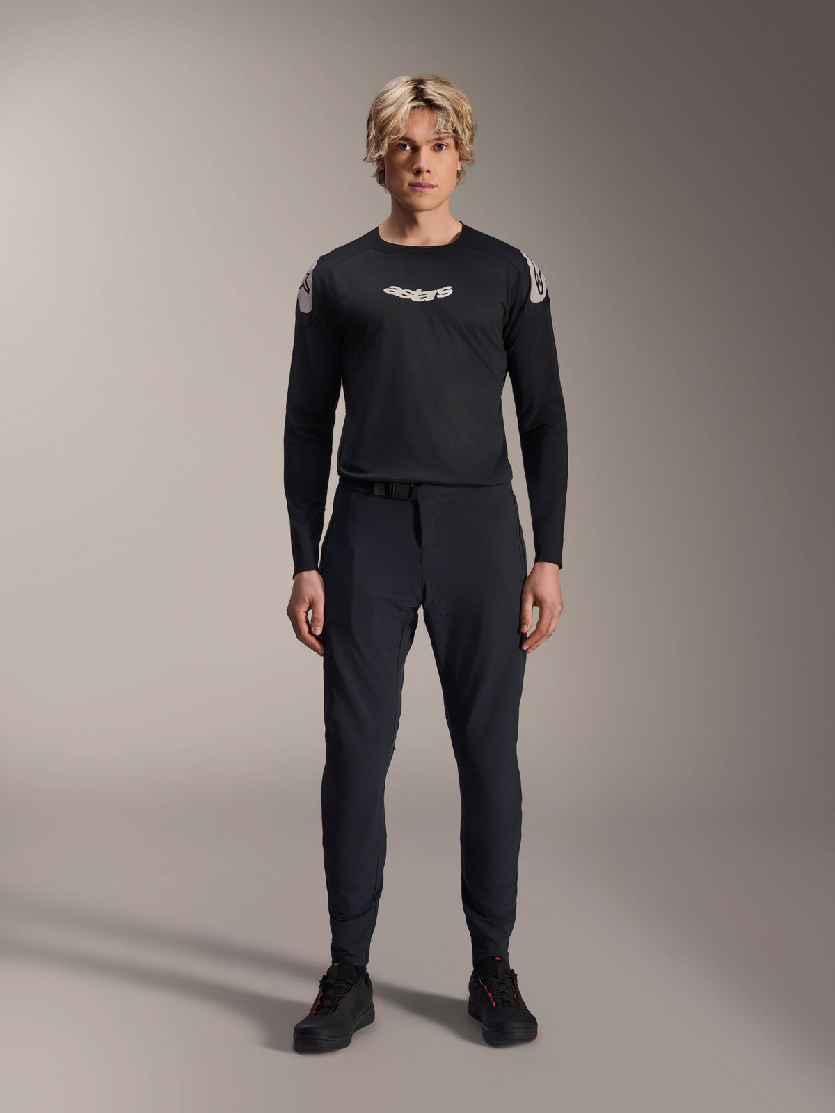 Manlig modell som bär Alpinestars A-Aria Polartec Elite långärmad tröja i svart, med en vit Astars-logotyp på bröstet och logotyper på axlarna, kombinerat med svarta tekniska MTB-byxor och skor, prestandautrustning för mountainbike