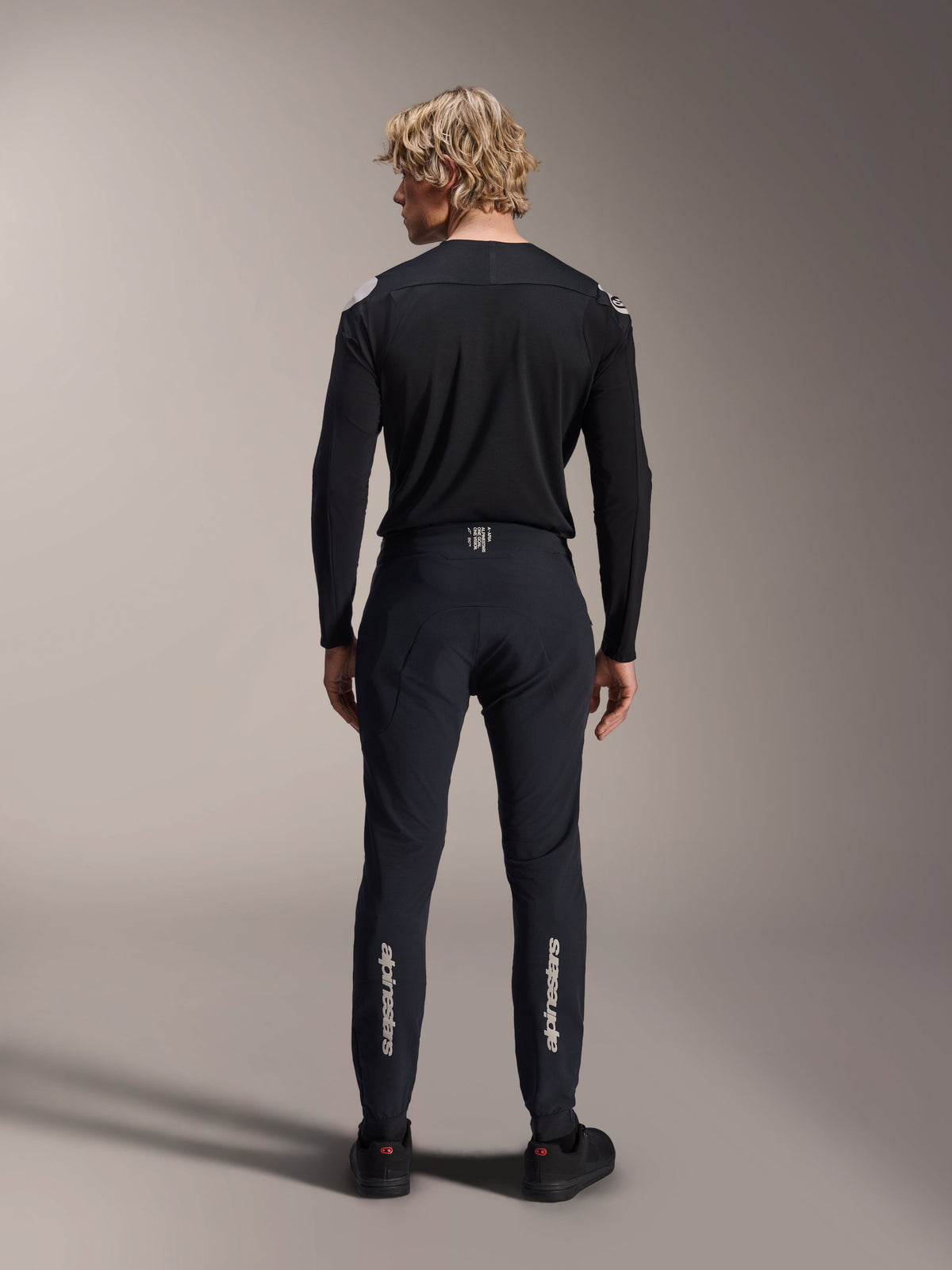 Alpinestars A-Aria Polartec Elite långärmad tröja, svart MTB-tröja, sedd bakifrån med matchande svarta byxor, prestandapassform för mountainbike, med tekniskt fukttransporterande material och diskret logotyp på nedre delen av ryggen