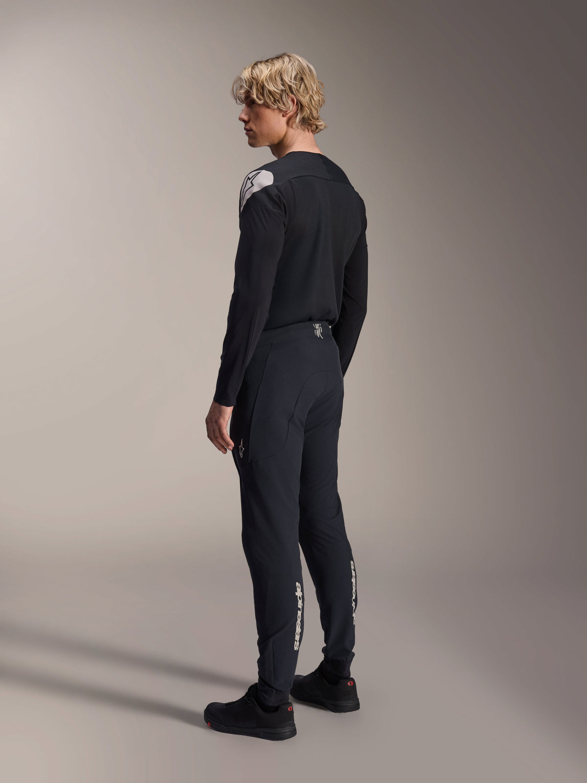 Alpinestars A-Aria Polartec Elite Jersey - långärmad, svart, buren av en modell i profil bakifrån, med en vit logotyp på axeln, kombinerad med matchande svarta cykelbyxor för en professionell MTB-outfit.